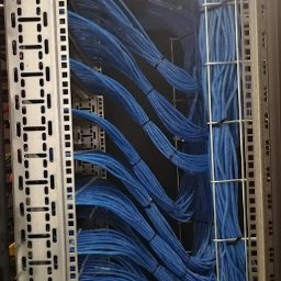 GUARD TECHNOLOGY SYSTEM MICHAŁ DĄBKOWSKI - Rząd szaf serwerowych z uporządkowanymi niebieskimi kablami sieciowymi, spiętymi czarnymi opaskami zaciskowymi, widoczne metalowe elementy konstrukcyjne szaf.