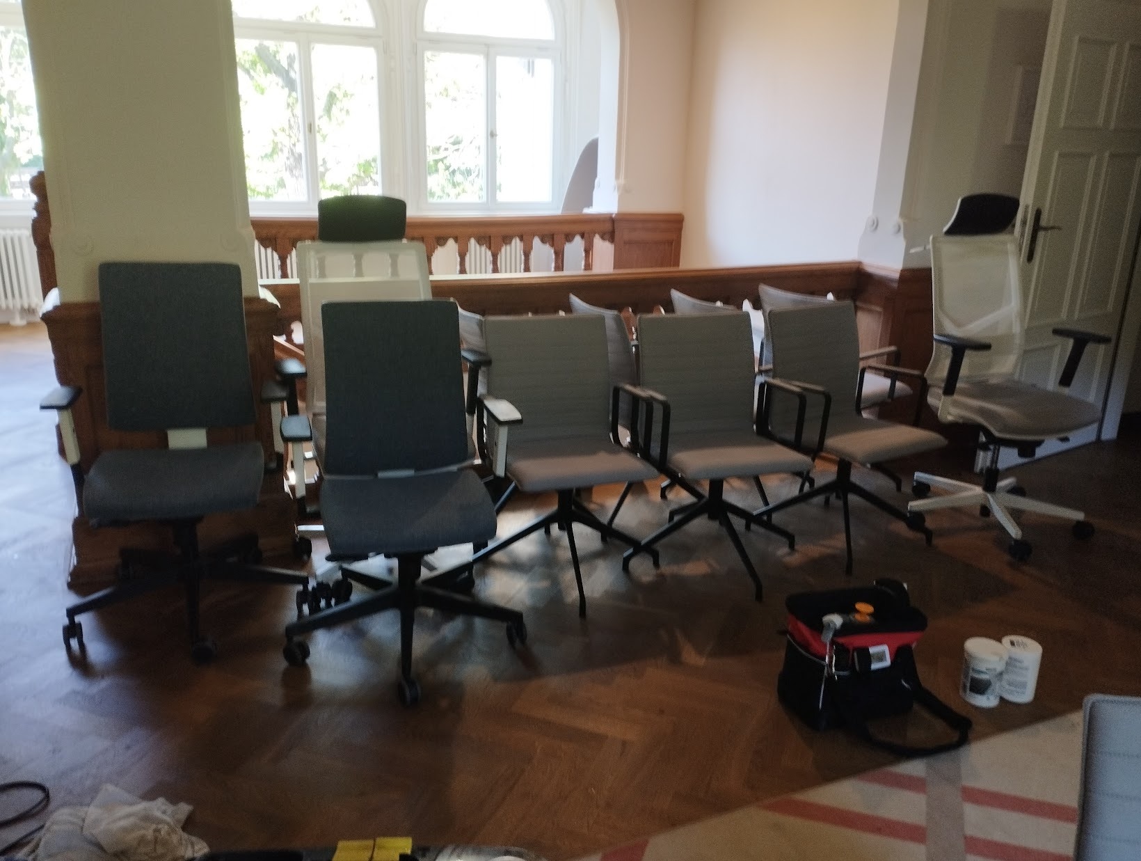 Przygotowane do czyszczenia biurowe krzesła na kółkach w jasnym pomieszczeniu z dużymi oknami, widoczny sprzęt do czyszczenia.