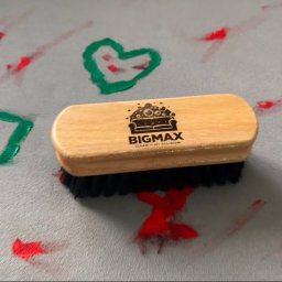 Władysław Kudriaszow BigMax Clean - Drewniana szczotka z czarnym włosiem i logo firmy BIGMAX na jasnoszarym dywanie z czerwonymi i zielonymi plamami farby w kształcie serca, kwadratu i innych wzorów.
