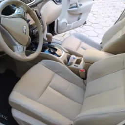 Jasna, skórzana tapicerka wnętrza samochodu Nissan X-Trail, widoczne fotele przednie, kierownica i deska rozdzielcza.