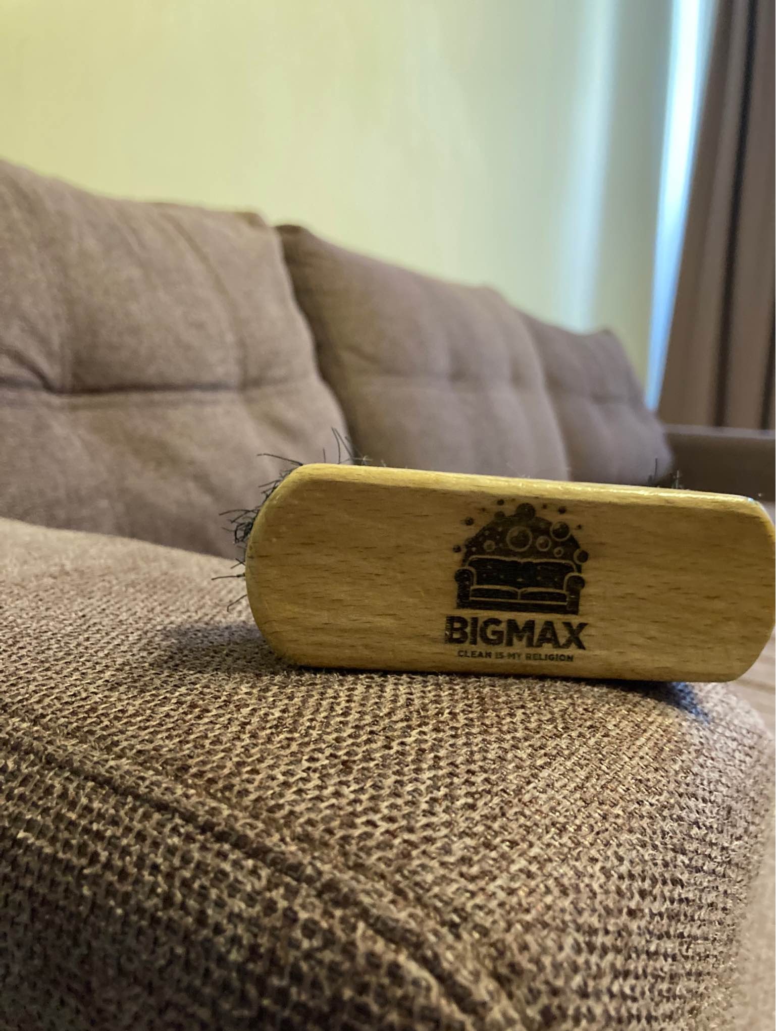Szczotka z logo BIGMAX leżąca na brązowej kanapie o wyraźnej strukturze tkaniny.