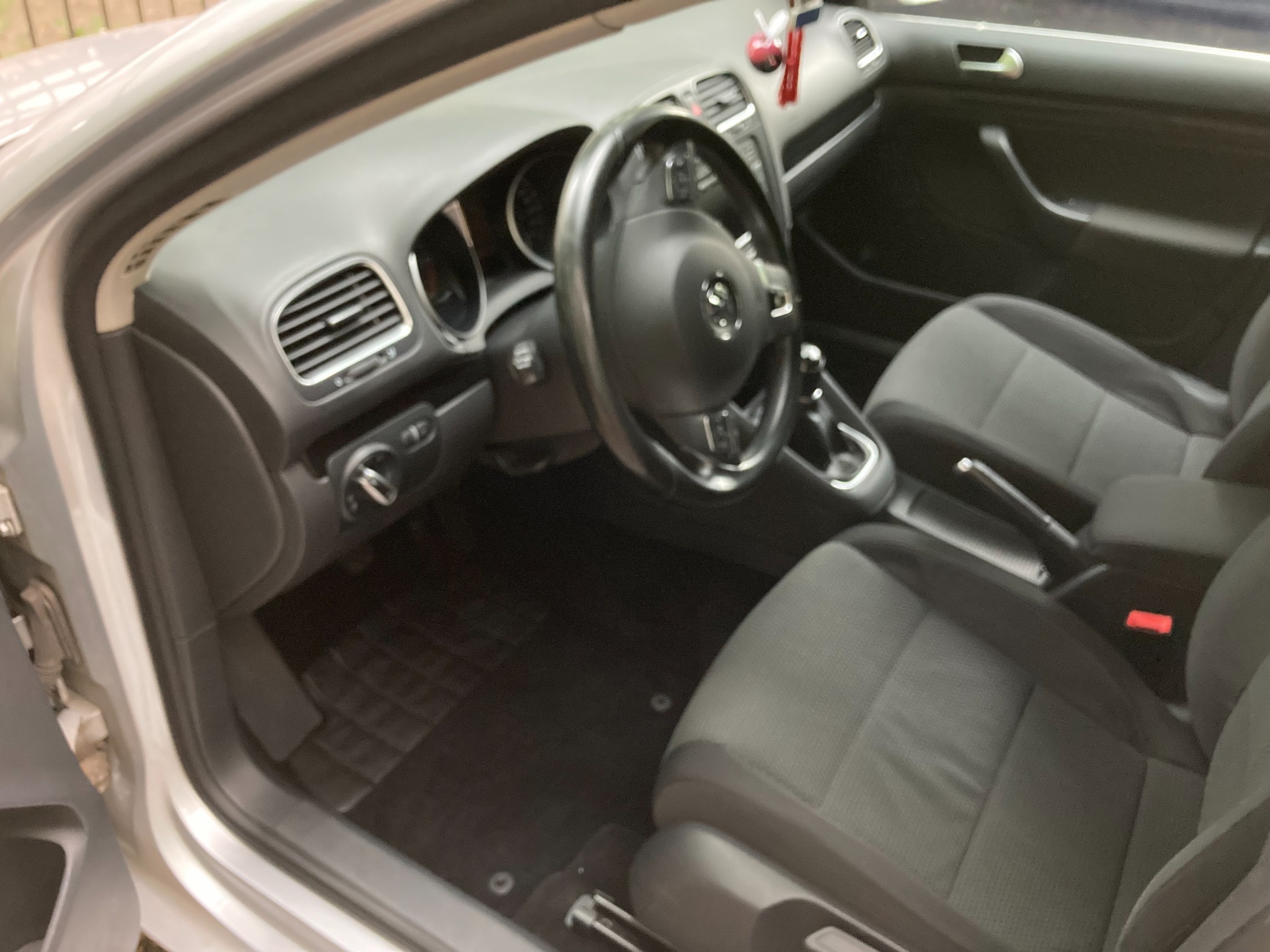 Wnętrze samochodu osobowego, widoczne przednie fotele z szarą tapicerką, deska rozdzielcza i kierownica z logo marki.