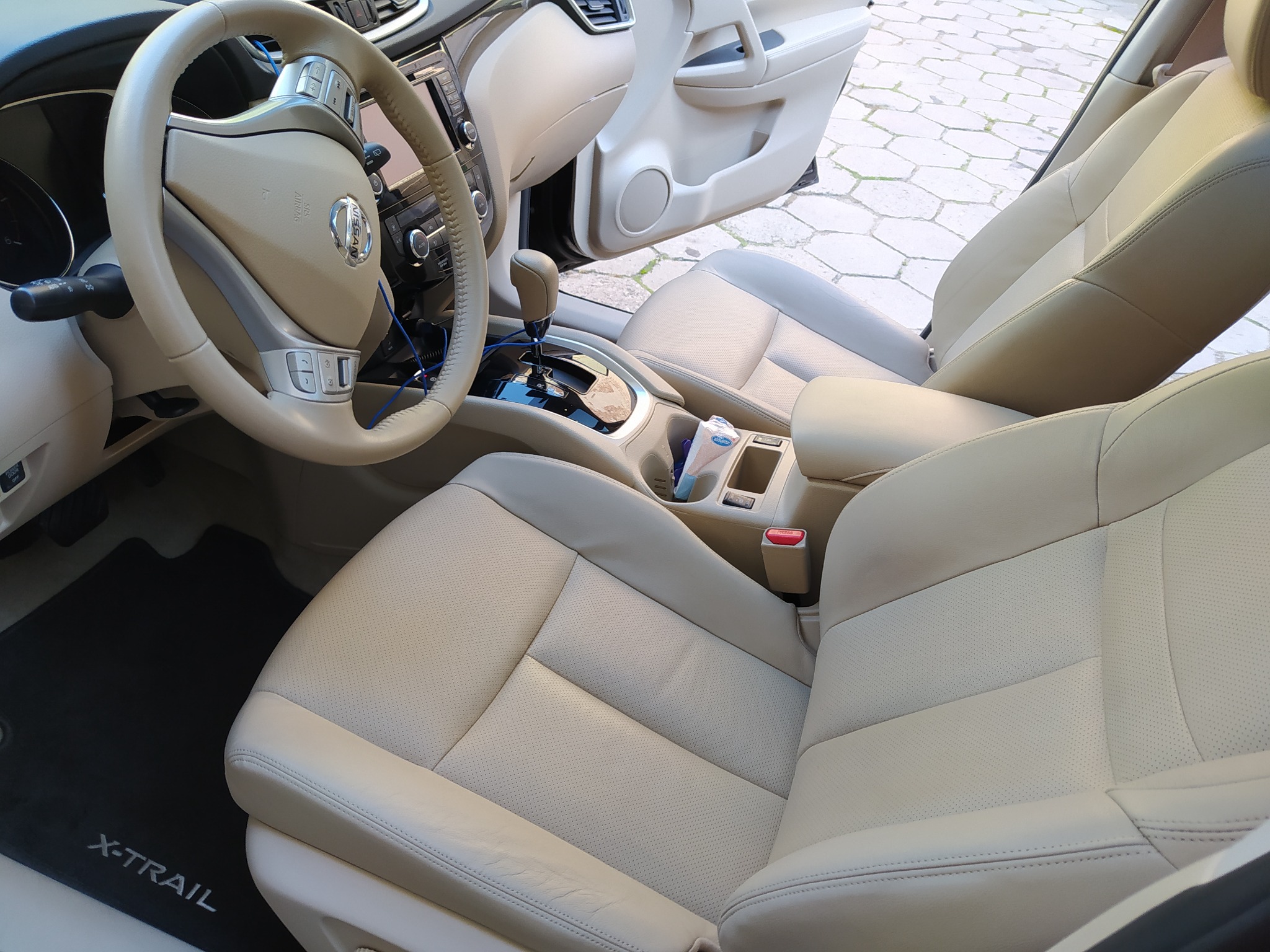 Jasna, skórzana tapicerka wnętrza samochodu Nissan X-Trail, widoczne fotele przednie, kierownica i deska rozdzielcza.