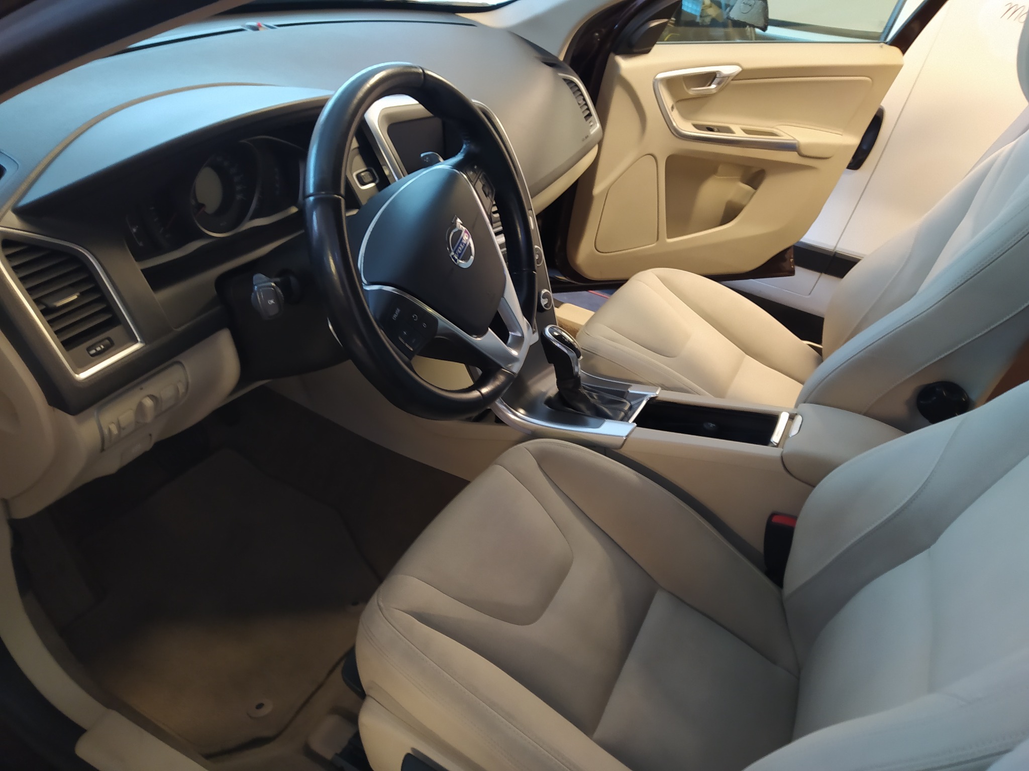 Wnętrze samochodu marki Volvo z jasną, skórzaną tapicerką, widok na kierownicę, deskę rozdzielczą i przednie fotele.