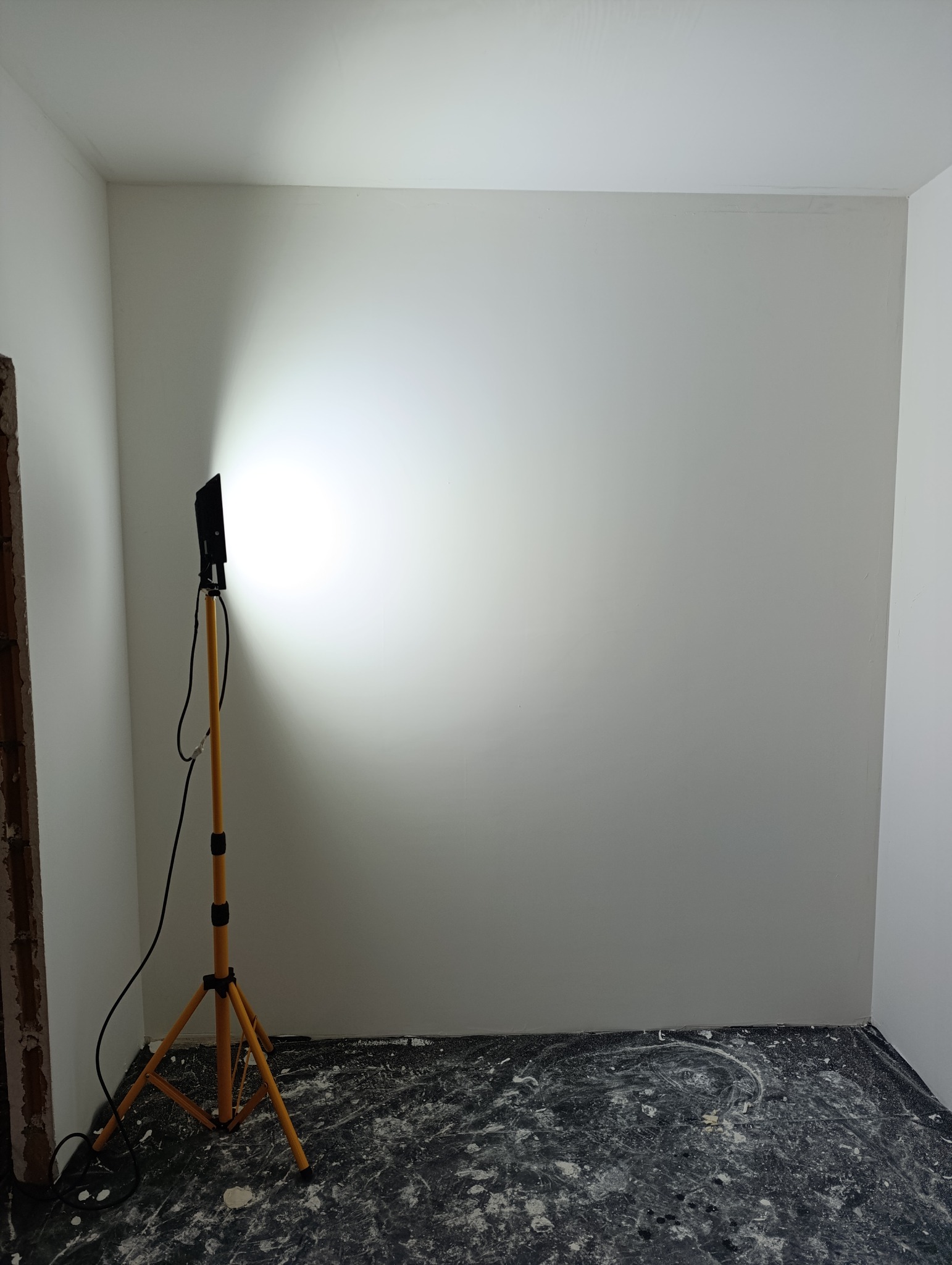 Świeżo pomalowane na biało wnętrze z widocznym halogenem budowlanym na statywie, podłoga zabezpieczona folią malarską z resztkami farby.