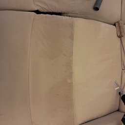 Loyal - Fragment beżowej kanapy z widoczną różnicą czystości po czyszczeniu, narzędzia do czyszczenia tapicerki w tle.