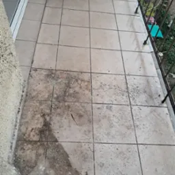 Kafelki na balkonie częściowo wyczyszczone, widoczna różnica w zabrudzeniu, fragment balustrady i klimatyzatora.
