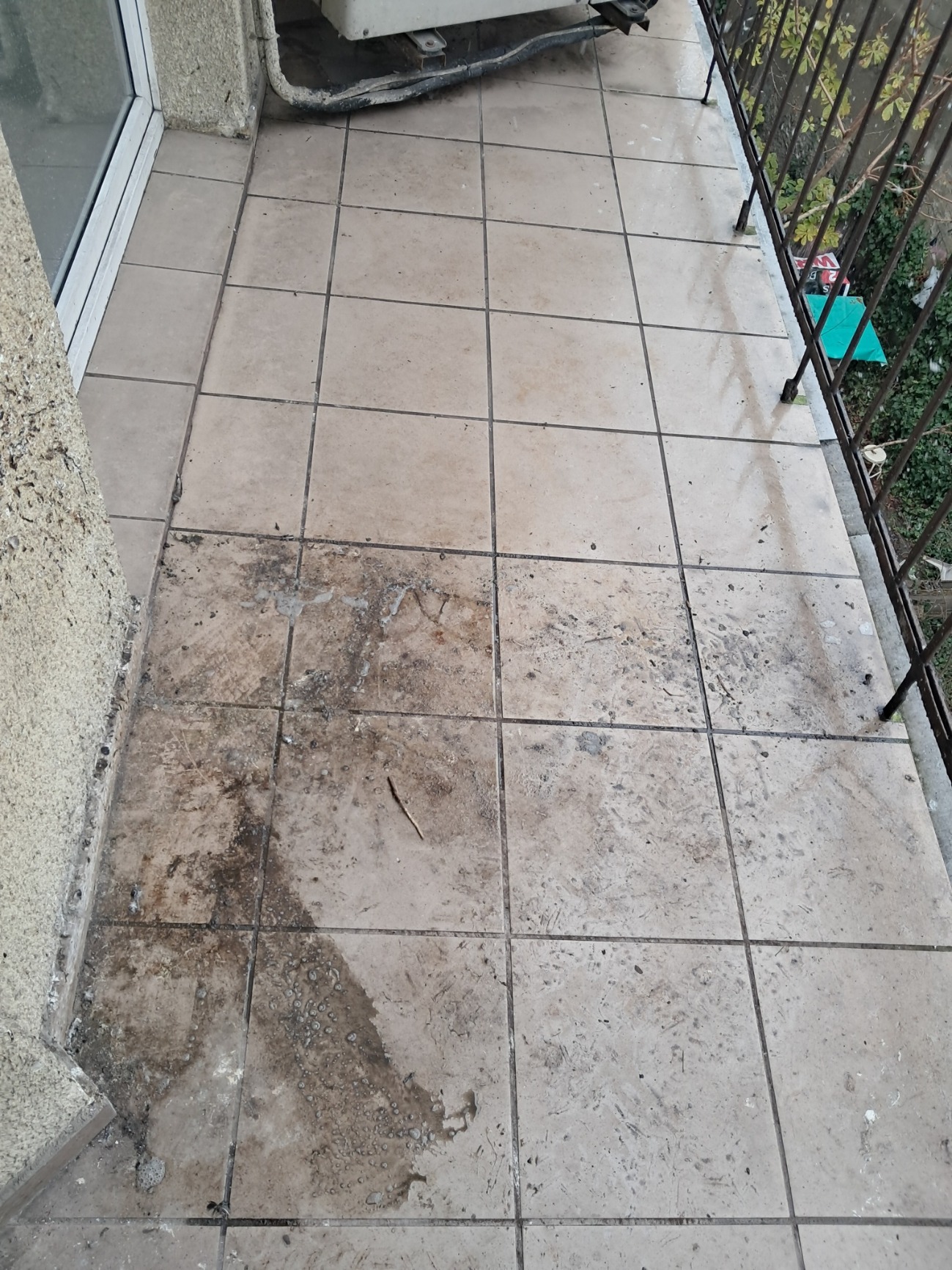 Kafelki na balkonie częściowo wyczyszczone, widoczna różnica w zabrudzeniu, fragment balustrady i klimatyzatora.