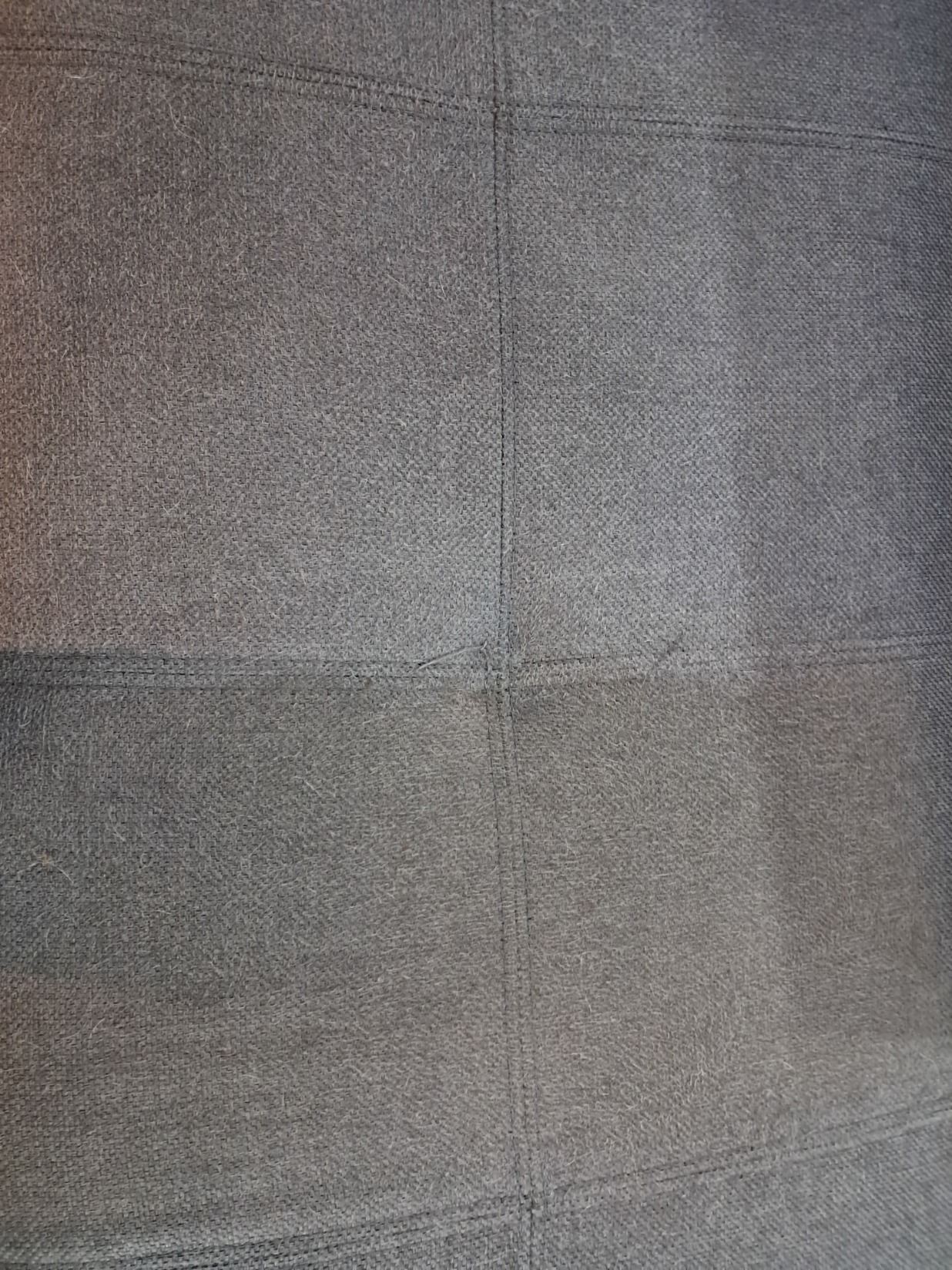 Zbliżenie na szarą, tekstylną tapicerkę z widocznymi szwami i drobnymi zabrudzeniami, sugerującymi potrzebę odświeżenia.