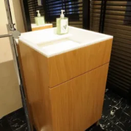 Nowoczesna umywalka z szafką z jasnego drewna, chromowana bateria stojąca i czarny marmur na podłodze, odbicie w lustrze z żaluzjami.