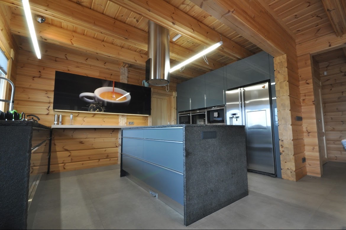 Nowoczesna kuchnia w drewnianym domu: szare fronty szafek, wyspa z blatem imitującym kamień, stalowa lodówka i okap, podświetlany panel z motywem filiżanki kawy.