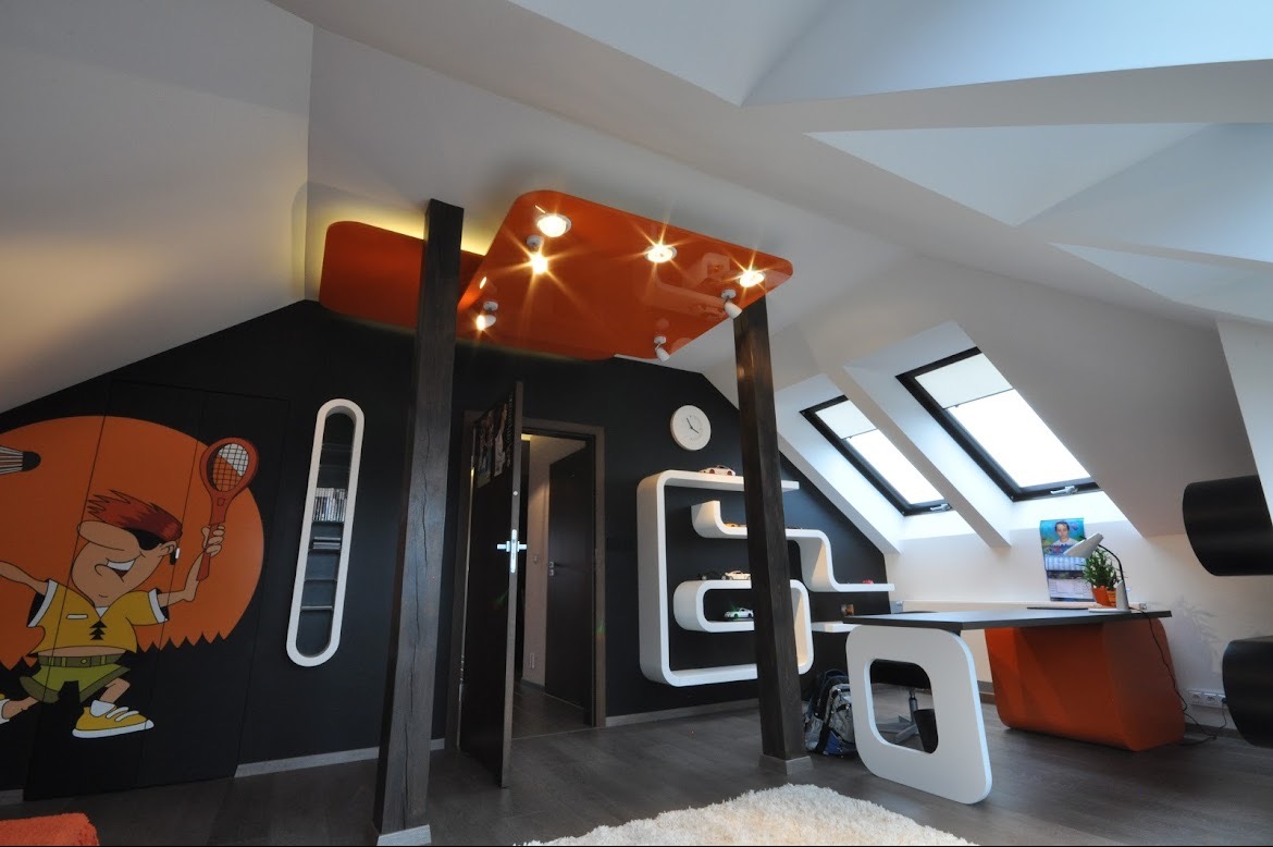 Pokój dziecięcy na poddaszu z czarną ścianą, pomarańczowymi akcentami, biurkiem, regałami w kształcie litery S i rysunkiem postaci z rakietą tenisową na szafie.