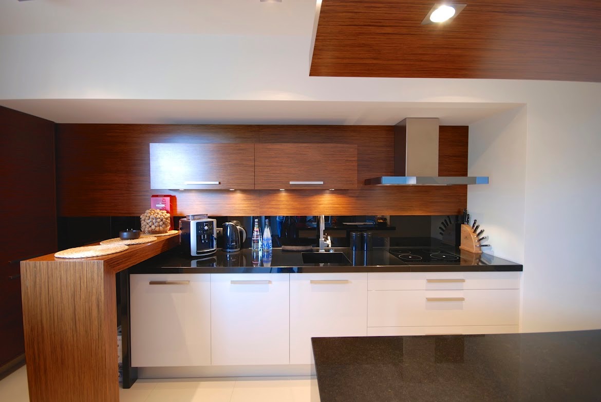 Nowoczesna kuchnia z białymi szafkami dolnymi i drewnianymi górnymi, czarny blat i lustrzany panel nad blatem, oświetlenie punktowe