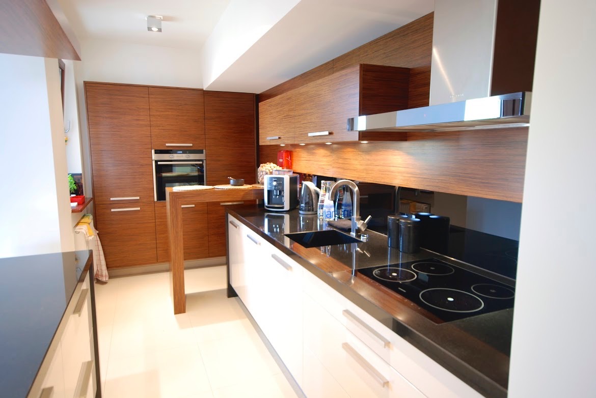 Nowoczesna kuchnia z drewnianymi frontami i czarnym blatem w Łodzi. Widoczny zlew, płyta indukcyjna oraz ekspres do kawy.