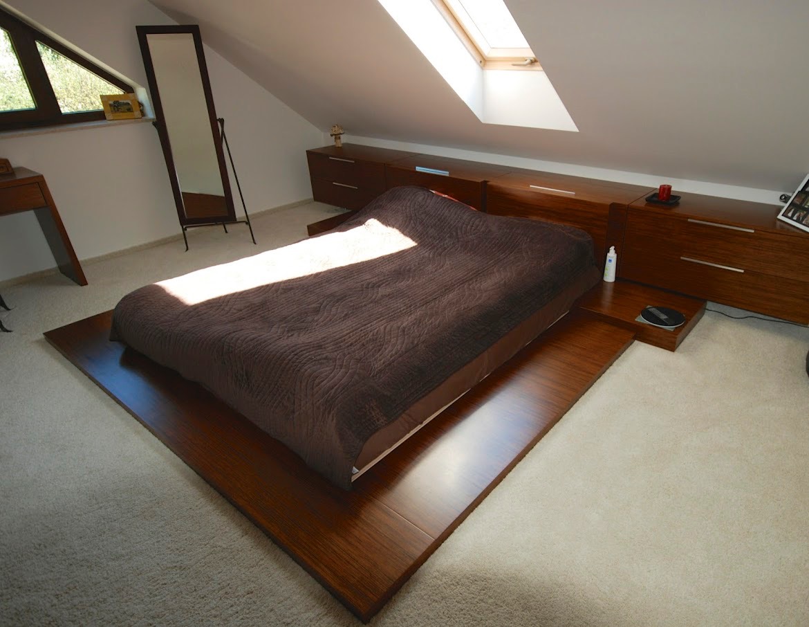 Minimalistyczna sypialnia na poddaszu z drewnianym łóżkiem na platformie, dopasowanymi szafkami nocnymi i oknem dachowym wpuszczającym jasne światło.