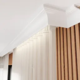 Dekoracyjna listwa przysufitowa z białego tworzywa sztucznego, zamontowana na styku sufitu i drewnianej ściany z pionowych paneli, z delikatną firanką w tle.