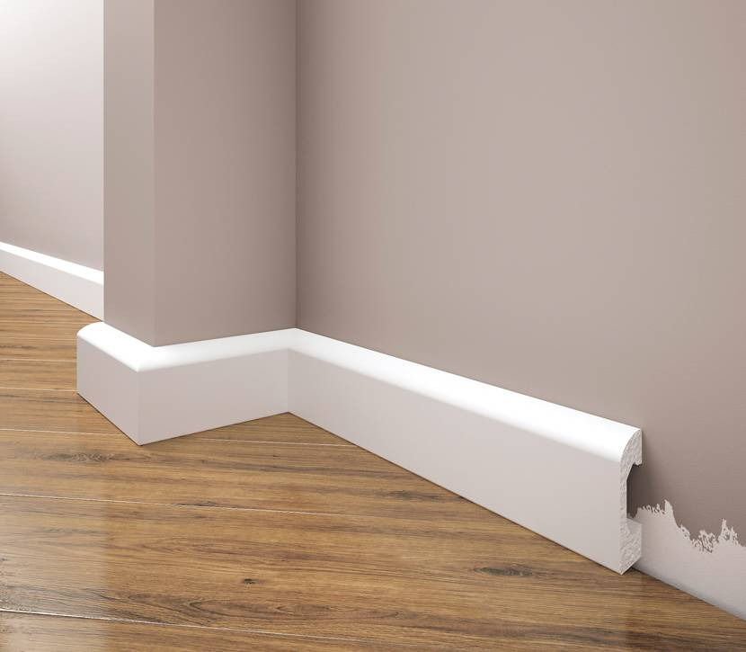 Biała listwa przypodłogowa zamontowana w rogu pomieszczenia na drewnianej podłodze, widoczny profil listwy.