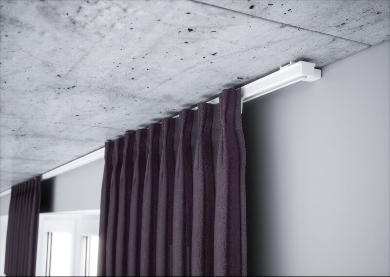 Zasłony w kolorze śliwkowym zawieszone na białym, sufitowym karniszu, na tle surowego, betonowego stropu.