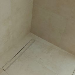 Damian Kwieciński - Beżowa kabina prysznicowa z odpływem liniowym i chromowaną armaturą, wykończona płytkami imitującymi kamień.