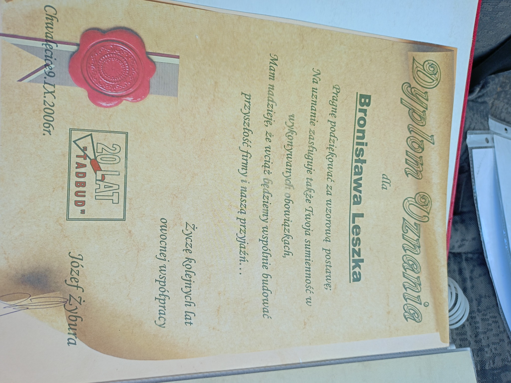 Dyplom Uznania dla Bronisława Leszka od firmy Tadbud, z pieczęcią i podpisem Józefa Żybura, datowany na 9 września 2006 roku, leżący na szarym tle.