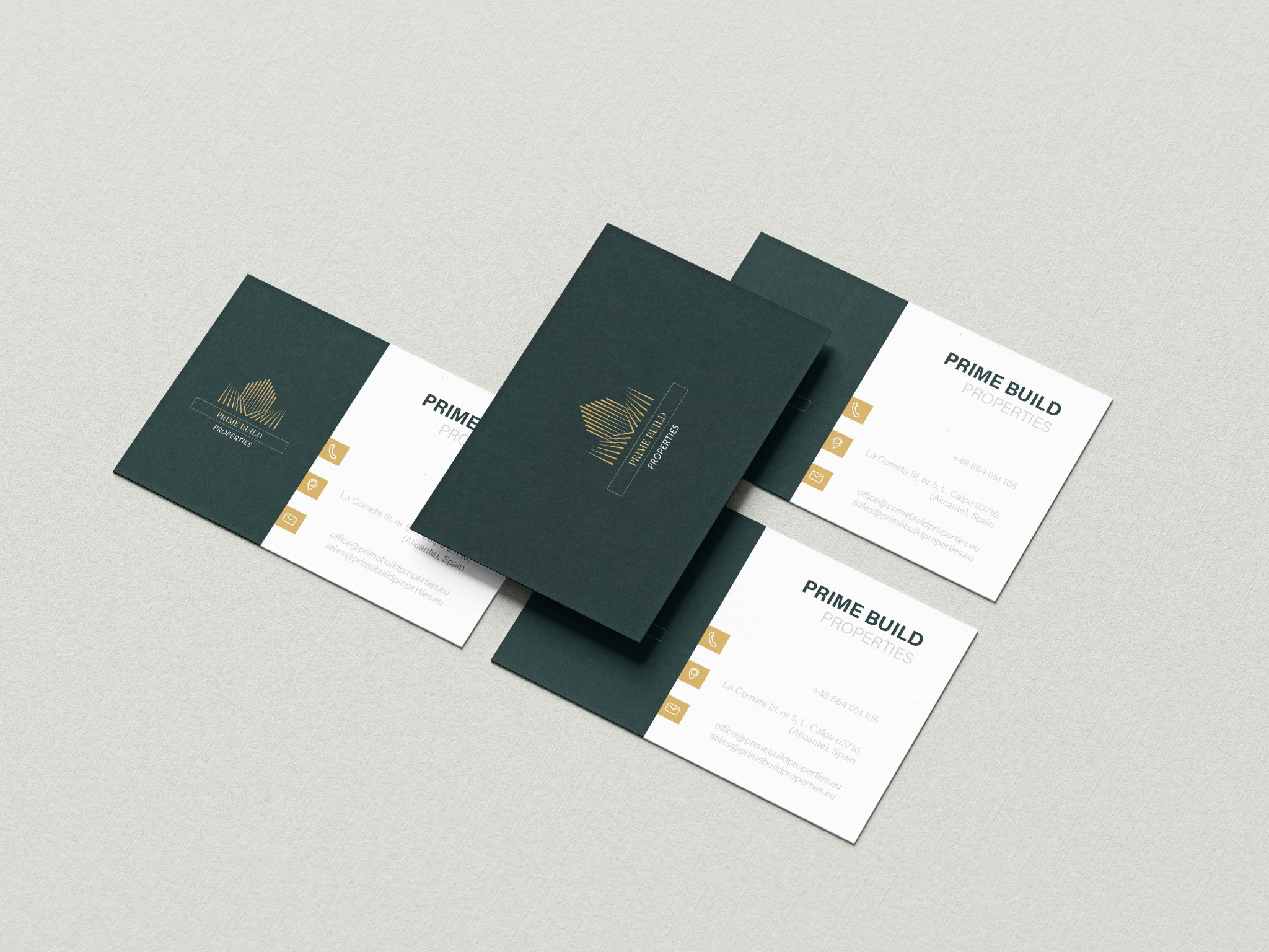 Zestaw wizytówek firmy Prime Build Properties w kolorach białym i ciemnozielonym ze złotym logo na teksturowanym, jasnoszarym tle.
