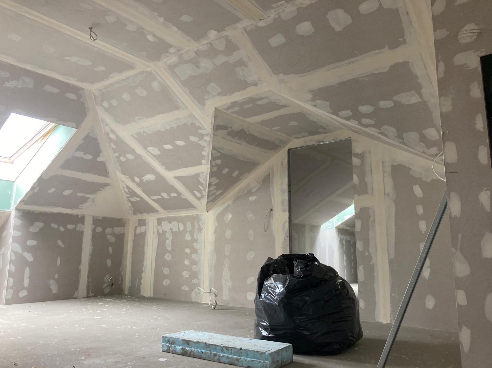 Poddasze po montażu płyt, szpachlowane łączenia widoczne, okno dachowe, worek na śmieci i płyta styropianowa na podłodze.