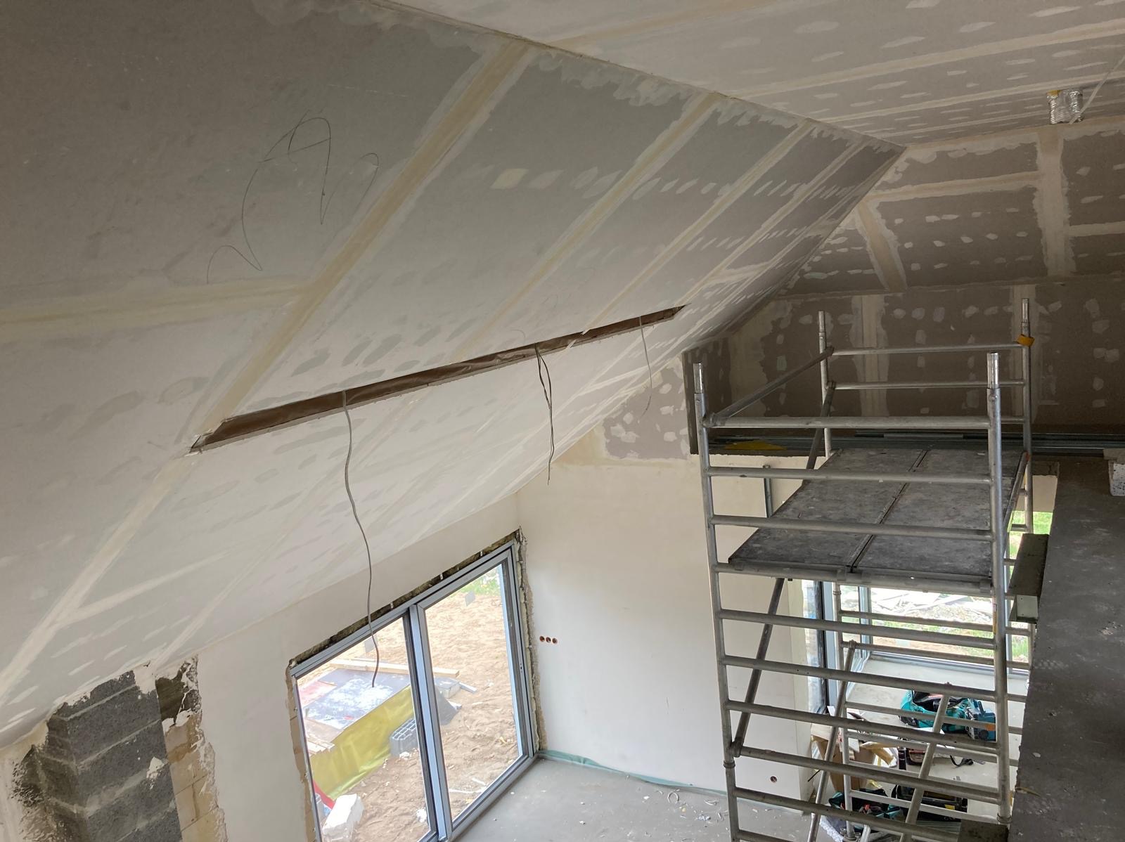 Montaż płyt na skośnym poddaszu w Bydgoszczy, widoczne rusztowanie i okno, częściowo wykończone ściany.