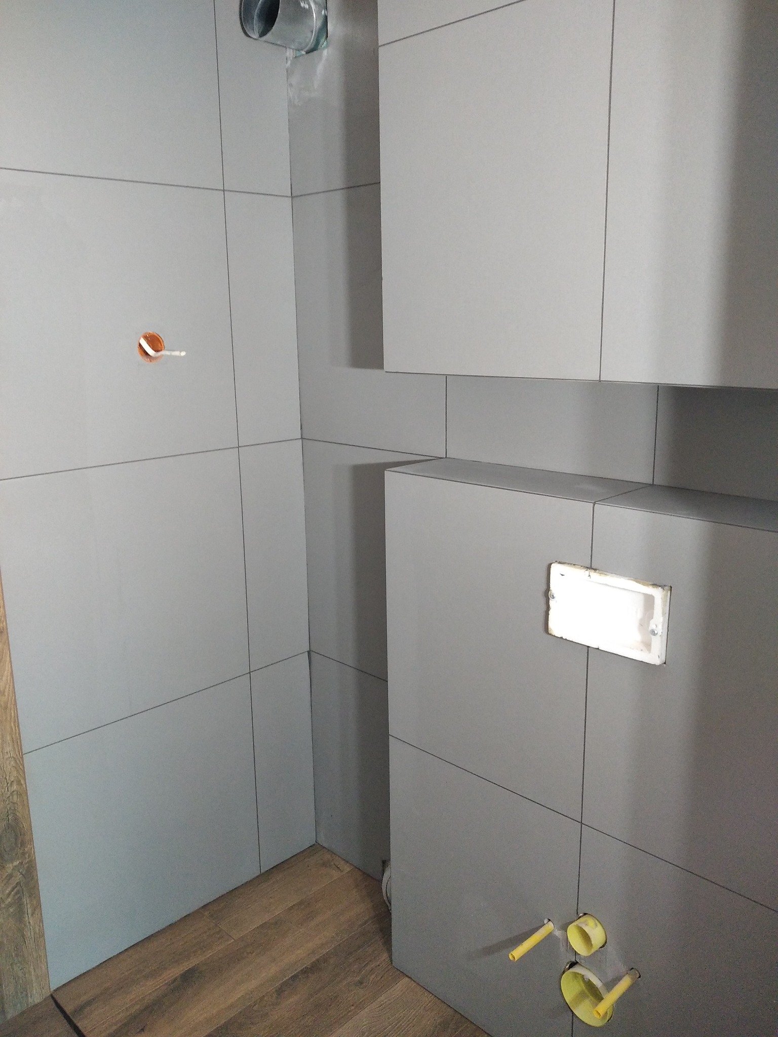 Szare płytki ścienne ułożone w łazience w Szczecinie, widoczne instalacje hydrauliczne i wentylacyjne przed montażem armatury.