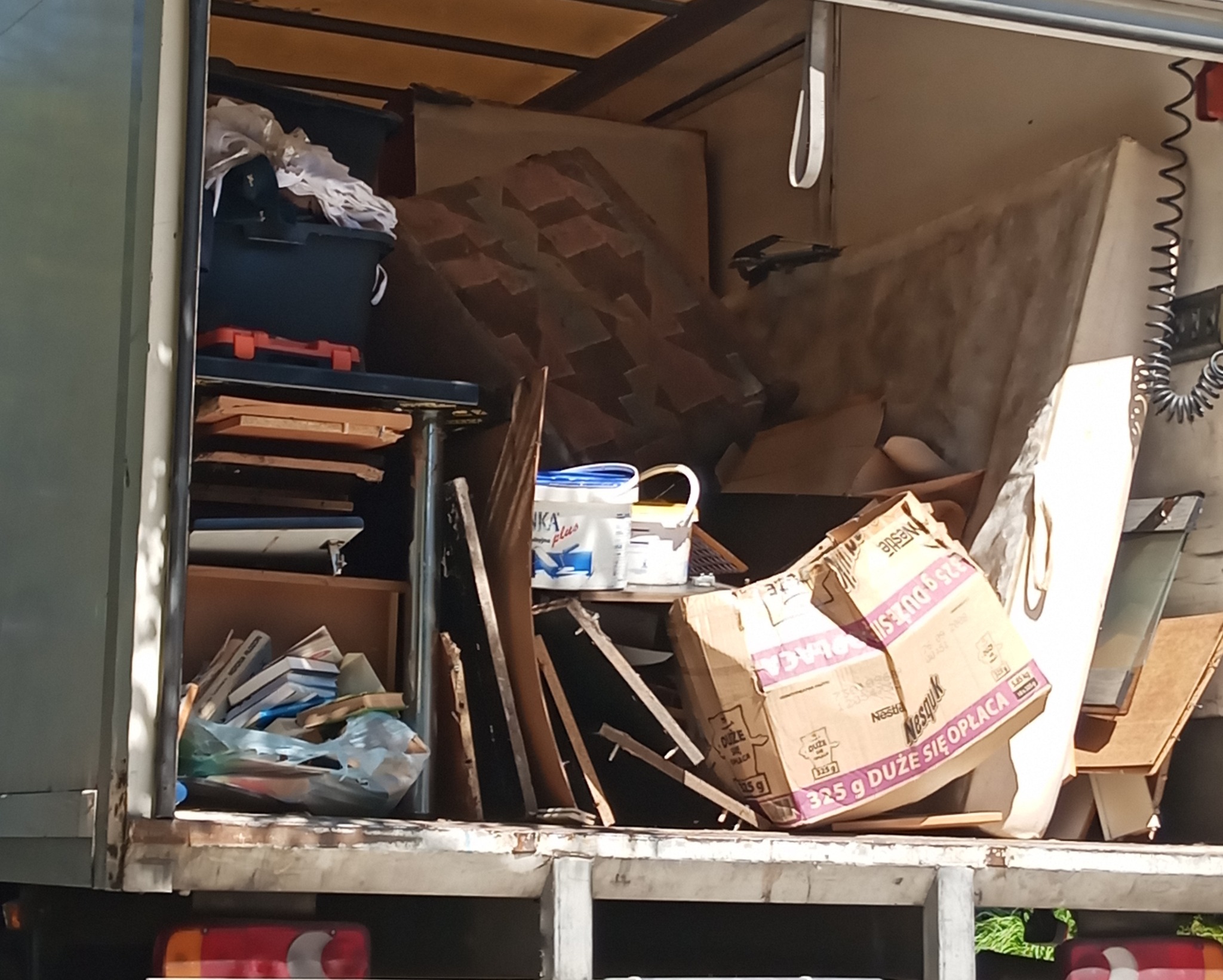 Wnętrze furgonetki wypełnionej różnorodnymi przedmiotami, w tym kartonami, wiadrami z farbą, książkami i elementami wyposażenia wnętrz, sugerujące usługę transportową lub opróżniania.