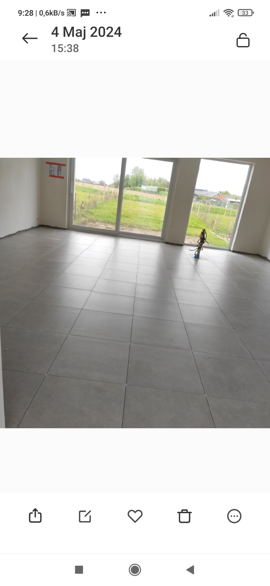 Wykończona podłoga z szarych płytek ceramicznych w nowym domu z widokiem na ogród przez przesuwne drzwi balkonowe. W rogu stoi narzędzie glazurnicze.