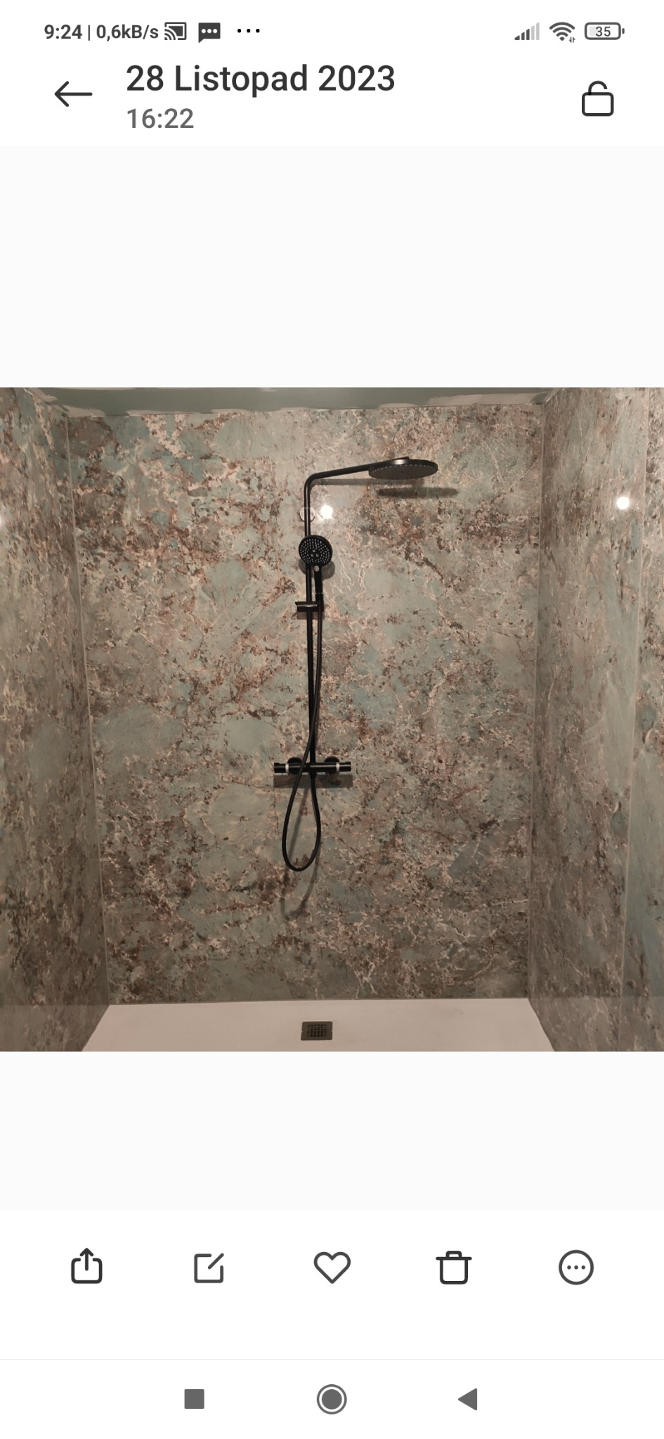 Ściana prysznicowa wykończona panelami imitującymi marmur w odcieniach szarości i błękitu, z zamontowaną czarną armaturą prysznicową.