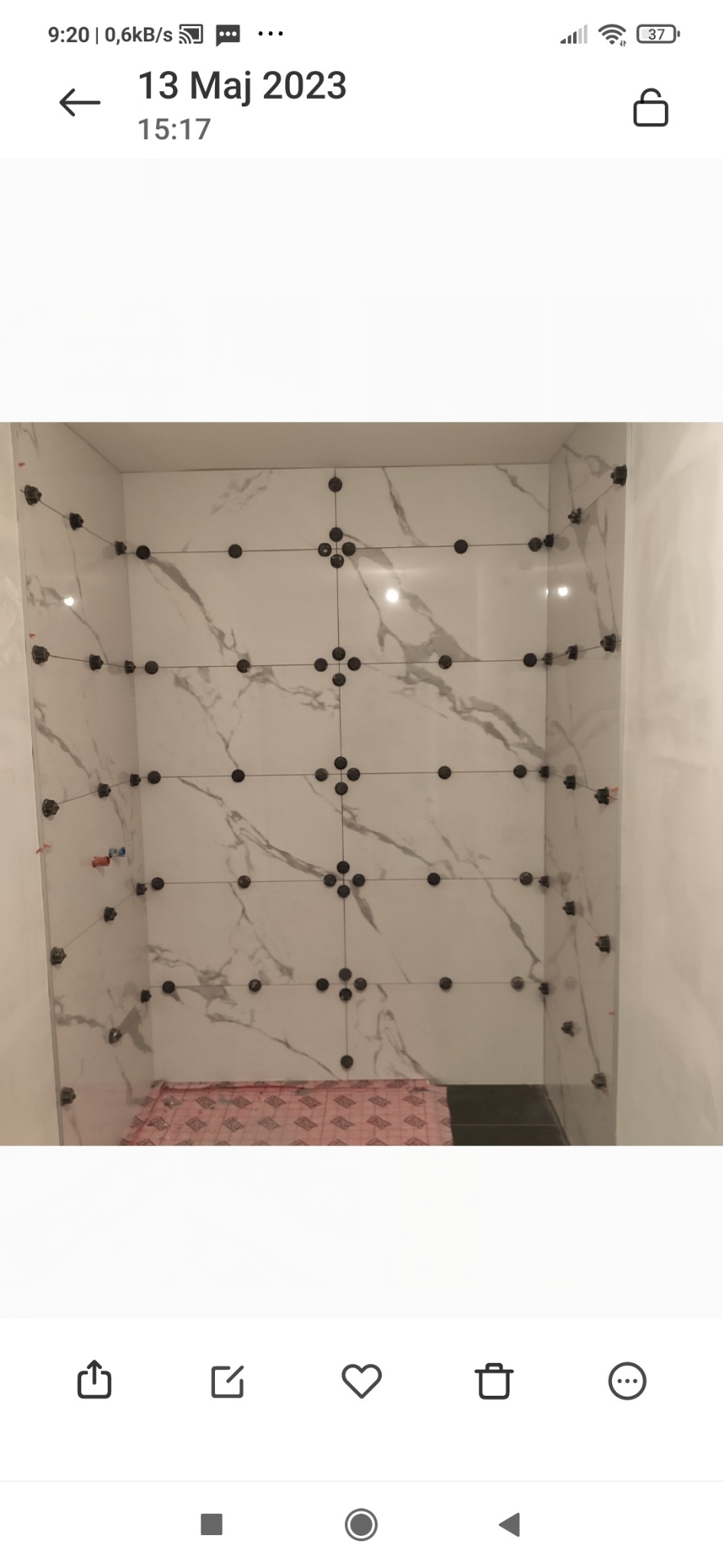 Białe płytki imitujące marmur, ułożone w kabinie prysznicowej, z czarnymi klipsami poziomującymi i krzyżykami dystansowymi, widoczny fragment maty izolacyjnej na podłodze.