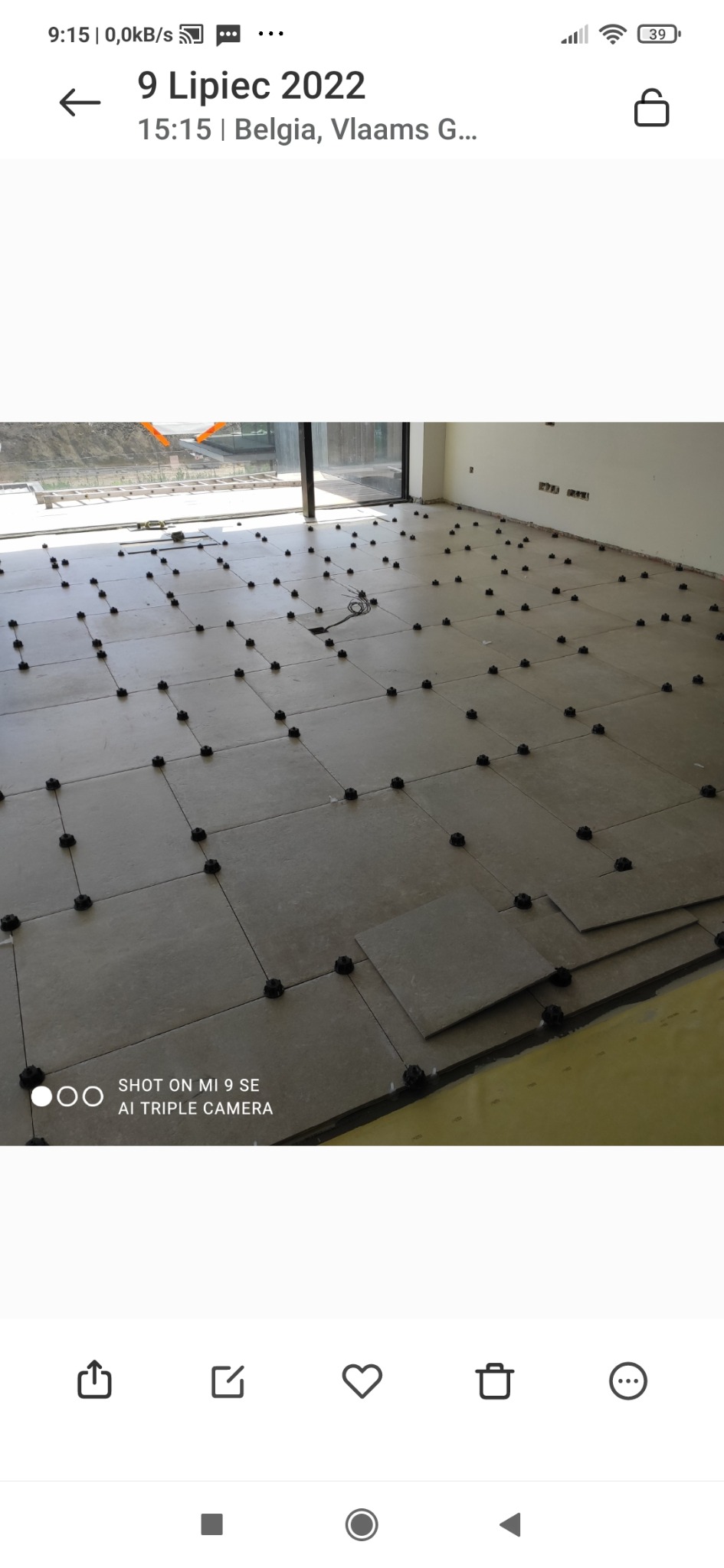 Układanie płytek podłogowych z użyciem systemu poziomowania, widoczne czarne klipsy dystansowe i częściowo ułożona podłoga w jasnych odcieniach szarości.