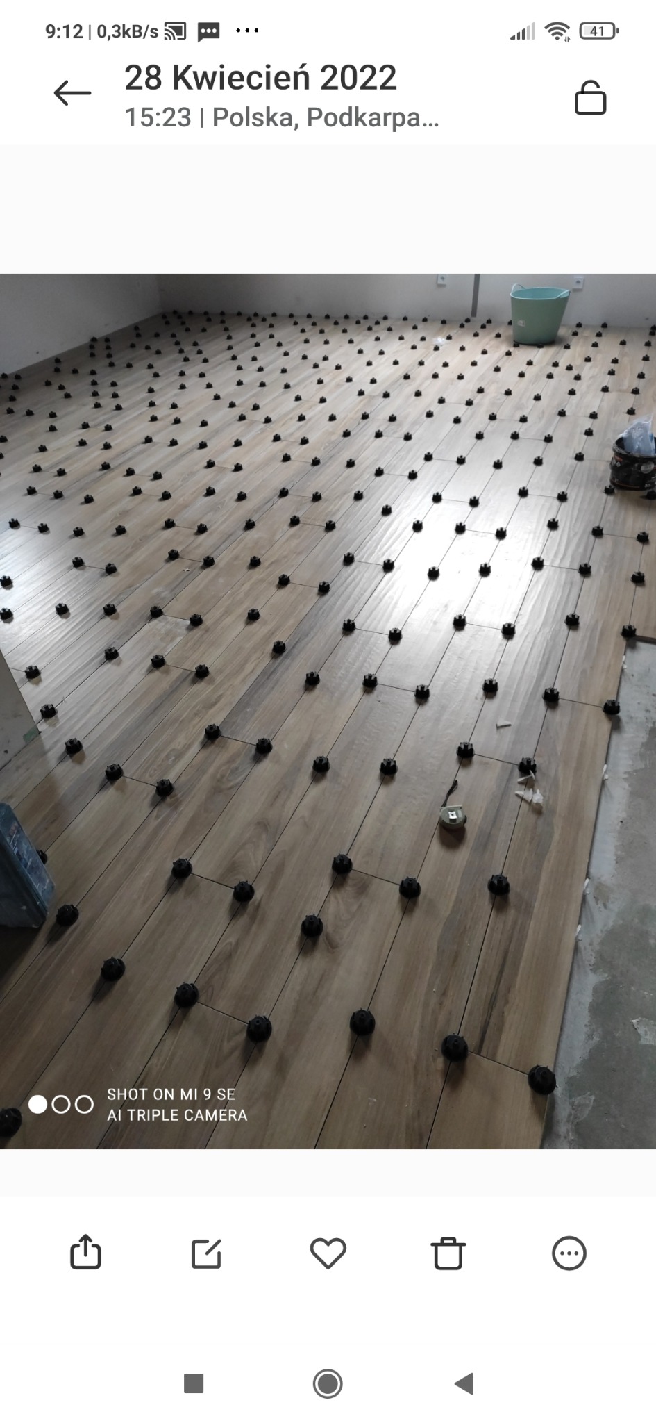 Układanie płytek podłogowych imitujących drewno z użyciem systemu poziomowania płytek, widoczny fragment ściany w stanie surowym.