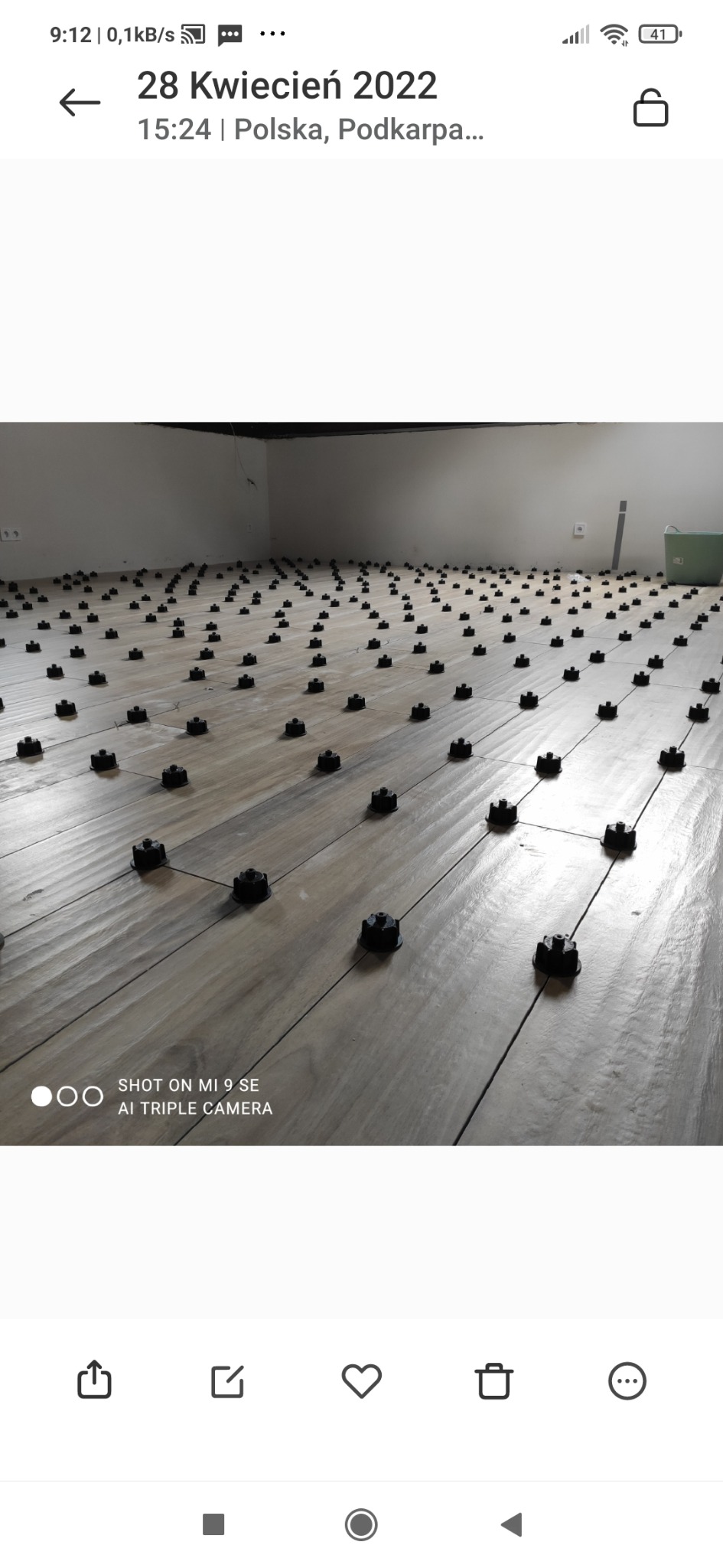 Układanie płytek podłogowych z użyciem systemu poziomowania, widoczne czarne klipsy i kliny na jasnych płytkach imitujących drewno.