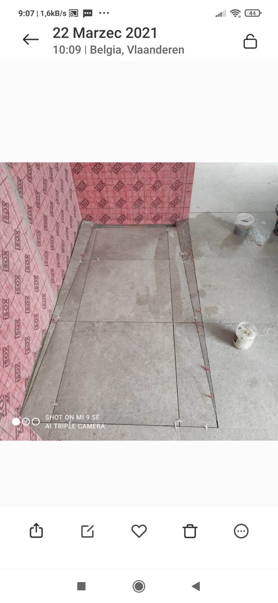 Przygotowanie do układania płytek na podłodze z zaznaczonym obszarem, widoczna izolacja ścienna i pojemnik z krzyżykami dystansowymi.