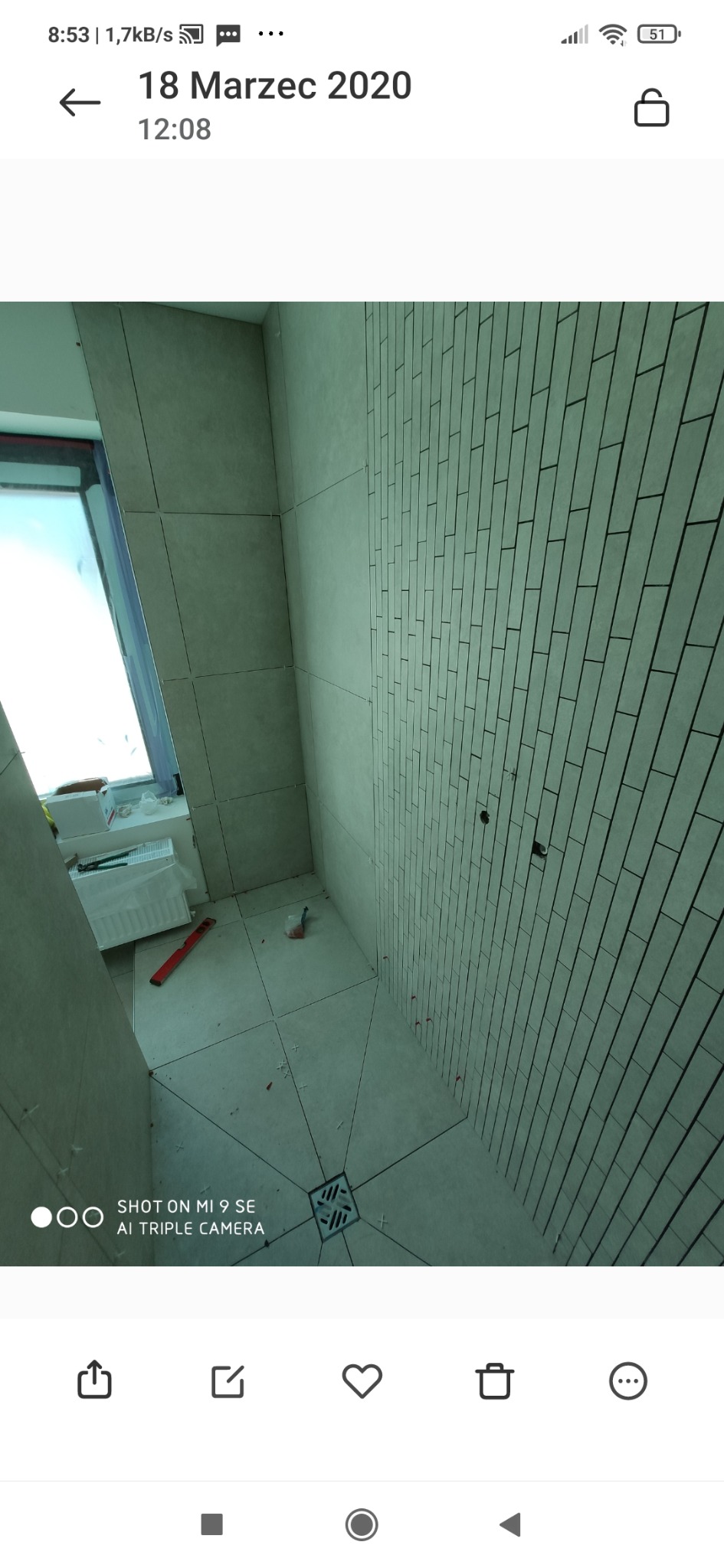 Wnętrze łazienki w trakcie układania płytek ceramicznych; widoczne płytki na ścianach w układzie cegiełki, płytki podłogowe z fugami, odpływ liniowy, poziomica oraz krzyżyki dystansowe.