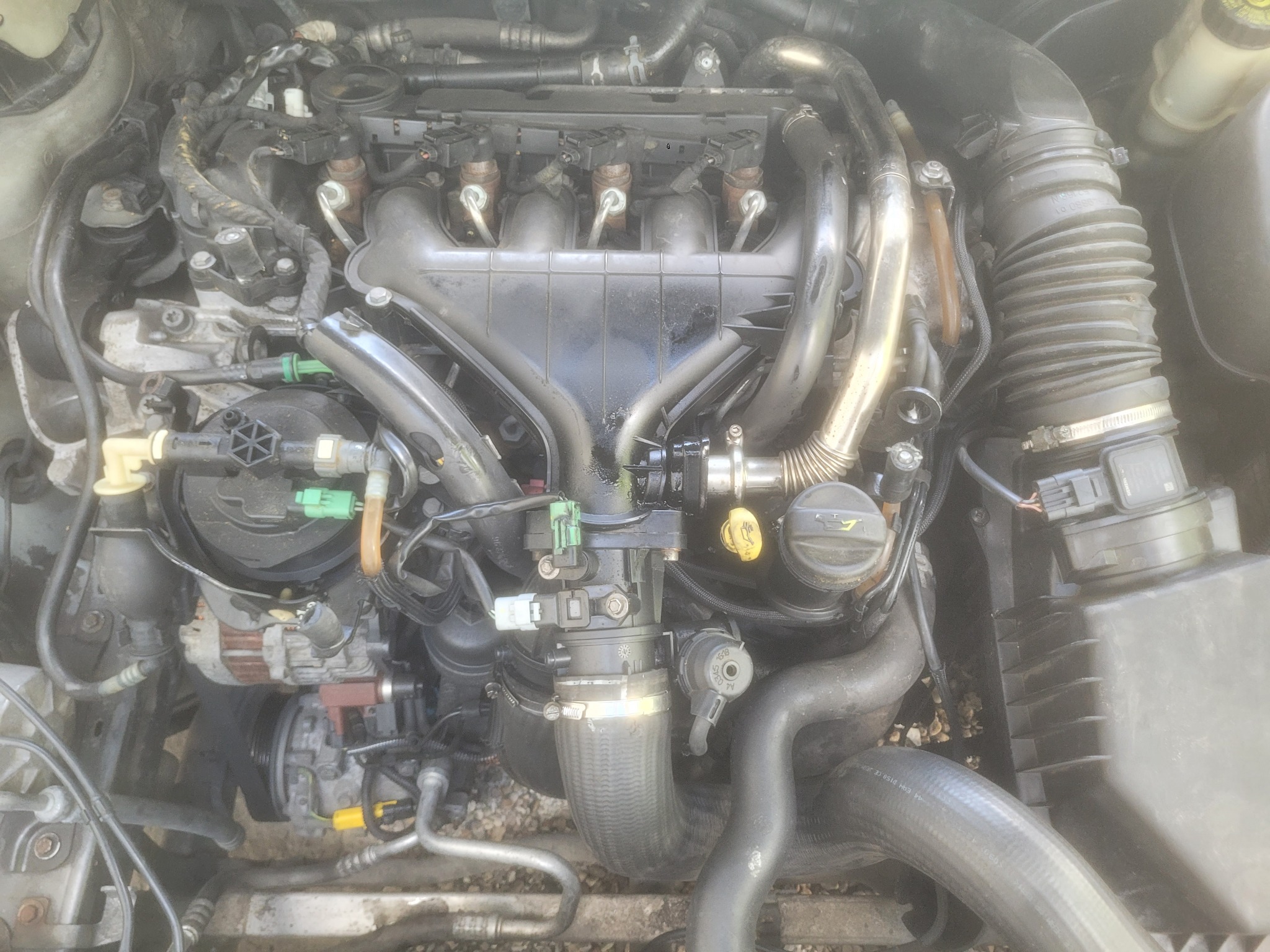 Widok z góry na silnik samochodowy z widocznymi przewodami, wtryskiwaczami i filtrami. Silnik jest lekko zabrudzony, a niektóre elementy wydają się być po konserwacji.