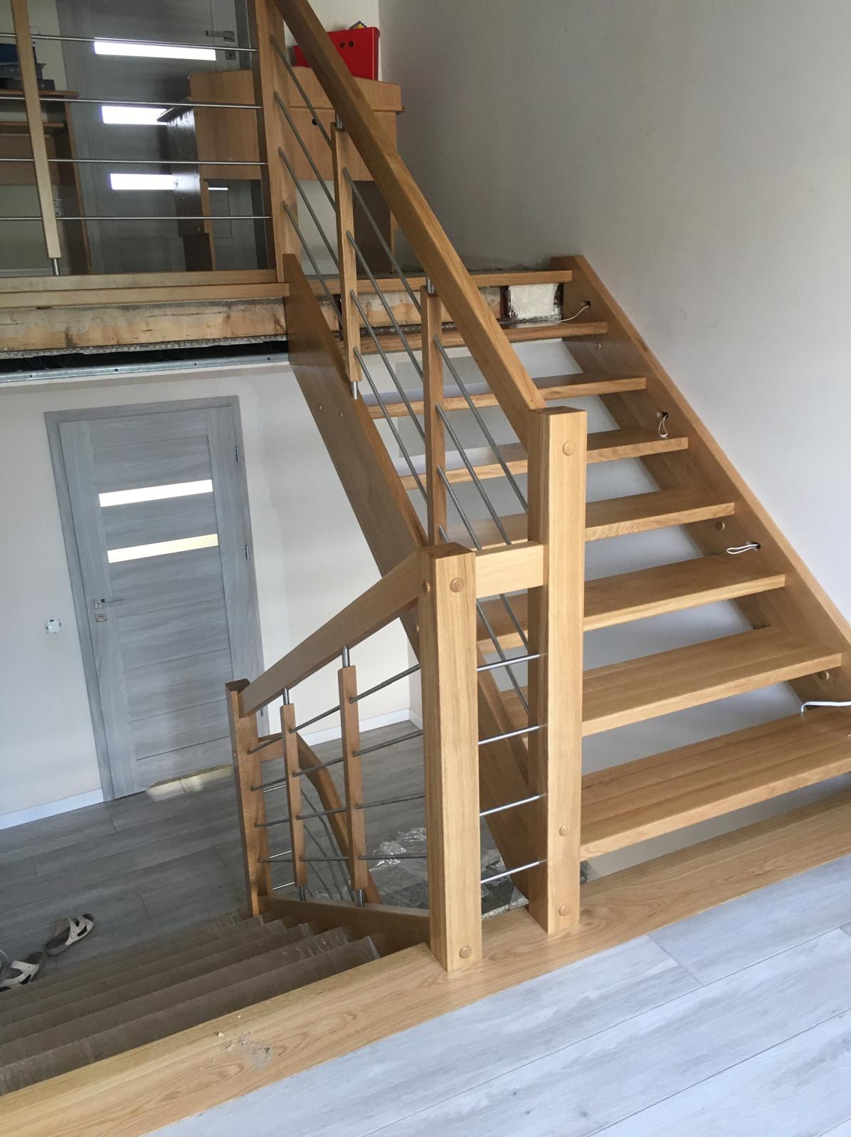 Jasne, ażurowe schody z drewnianymi stopniami i metalową balustradą, widoczne z dołu. Realizacja z Tworkowa. Minimalistyczny design.