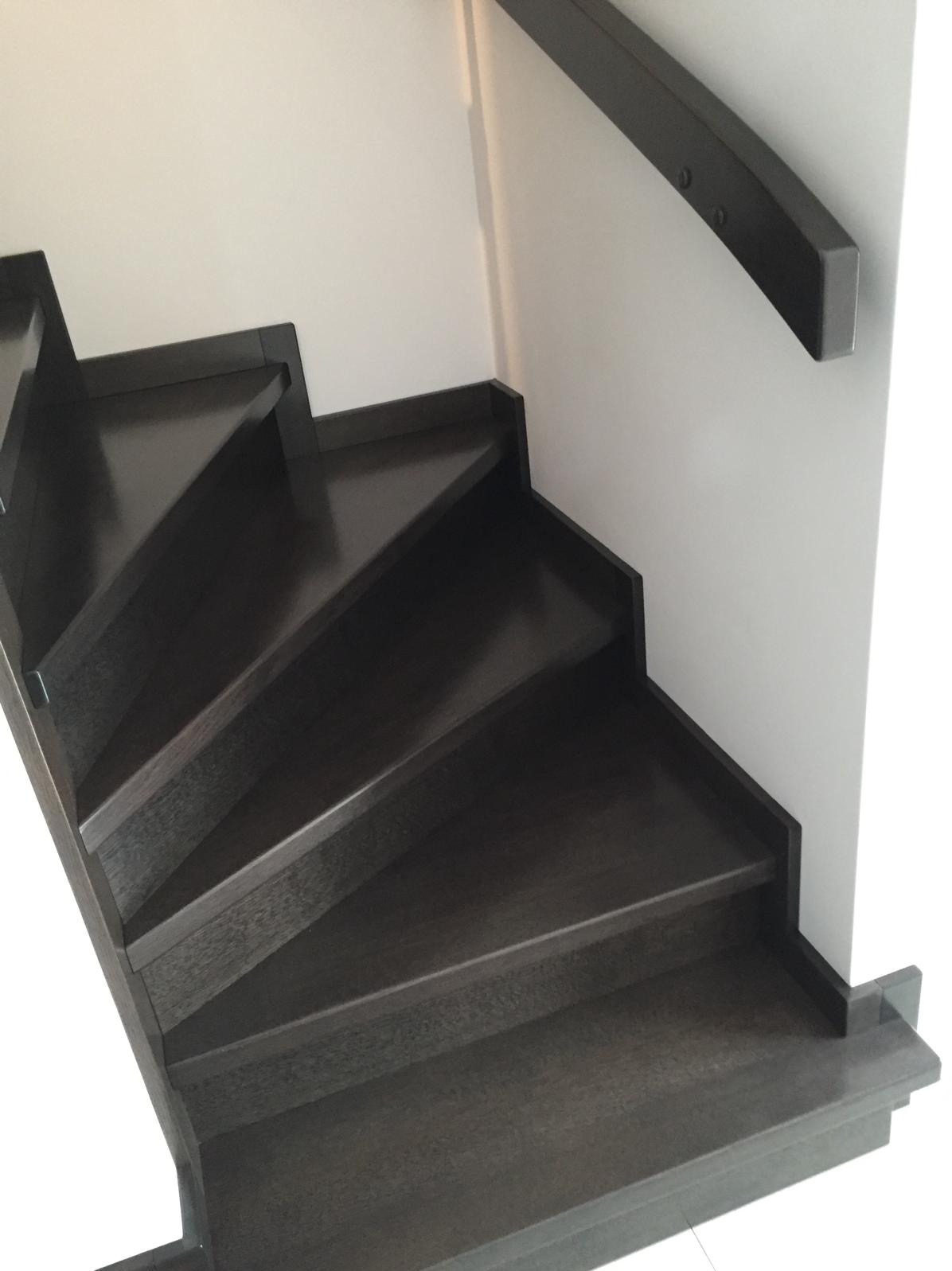 Nowoczesne schody z ciemnego drewna z minimalistyczną poręczą, widok z dołu, ukazujący precyzję wykonania i elegancki design. Schody prowadzą w górę, oświetlone naturalnym światłem.