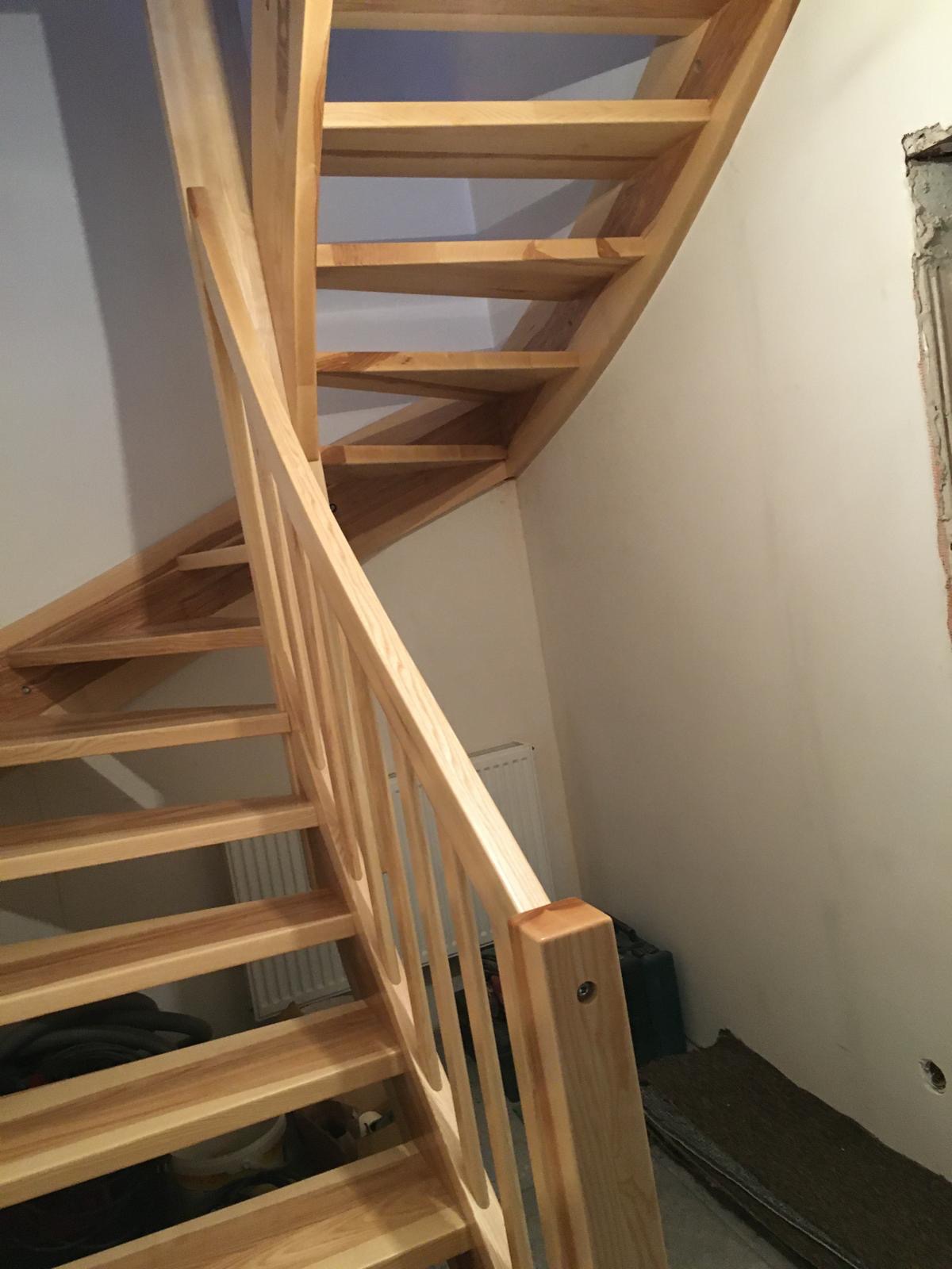 Jasne, spiralne schody z drewna z widoczną balustradą, prowadzące w górę w jasnym wnętrzu. Widoczne niedokończone wykończenia ścian i podłóg.