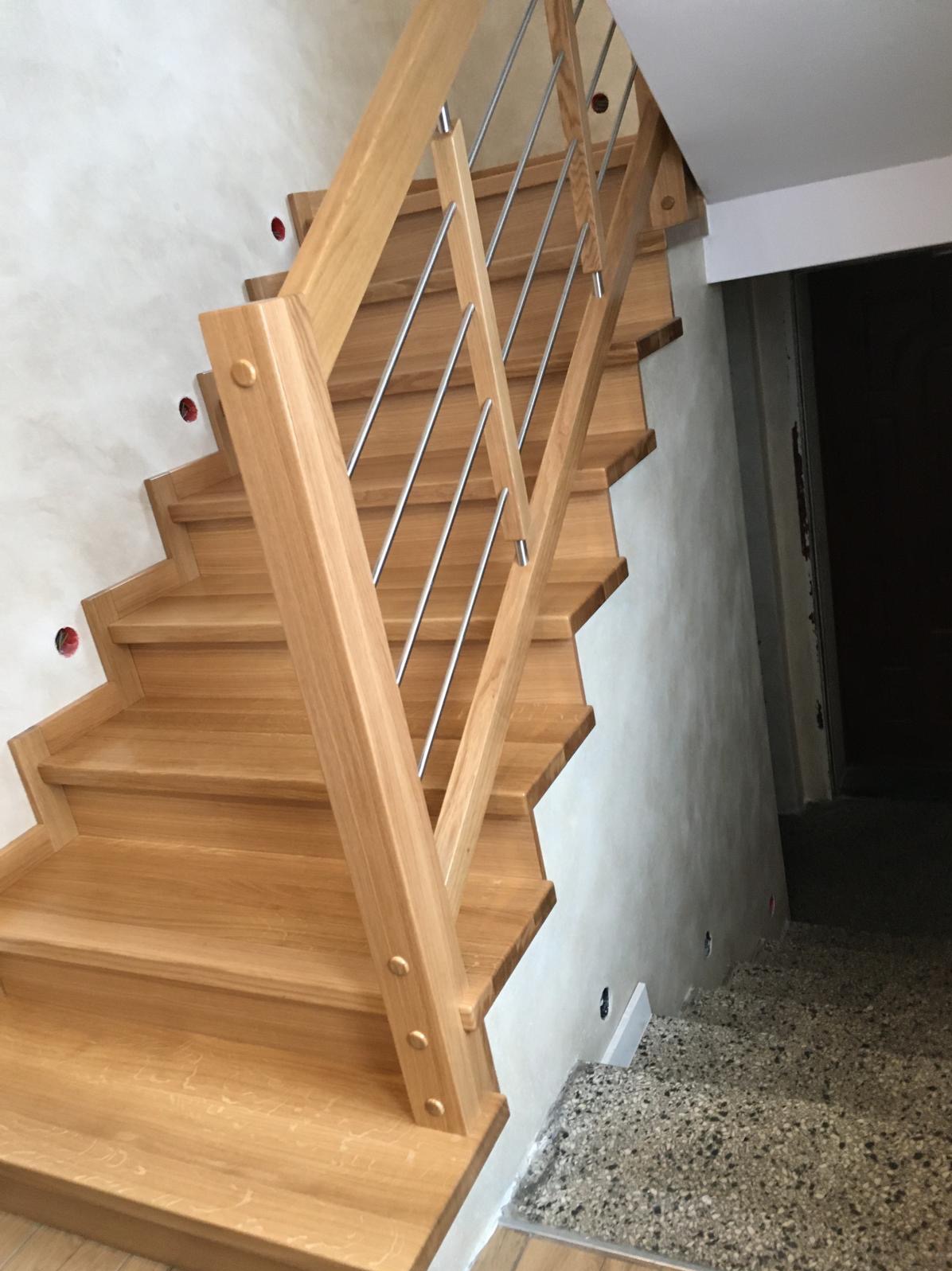 Jasne schody z drewna z metalową balustradą, widok z dołu. Charakterystyczne, zaokrąglone wykończenie stopni i minimalistyczny design balustrady.