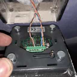 Podłączenie przewodów do listwy zaciskowej w module domofonu, widoczne elementy elektroniki na płytce drukowanej i fragment obudowy z czterema śrubami.