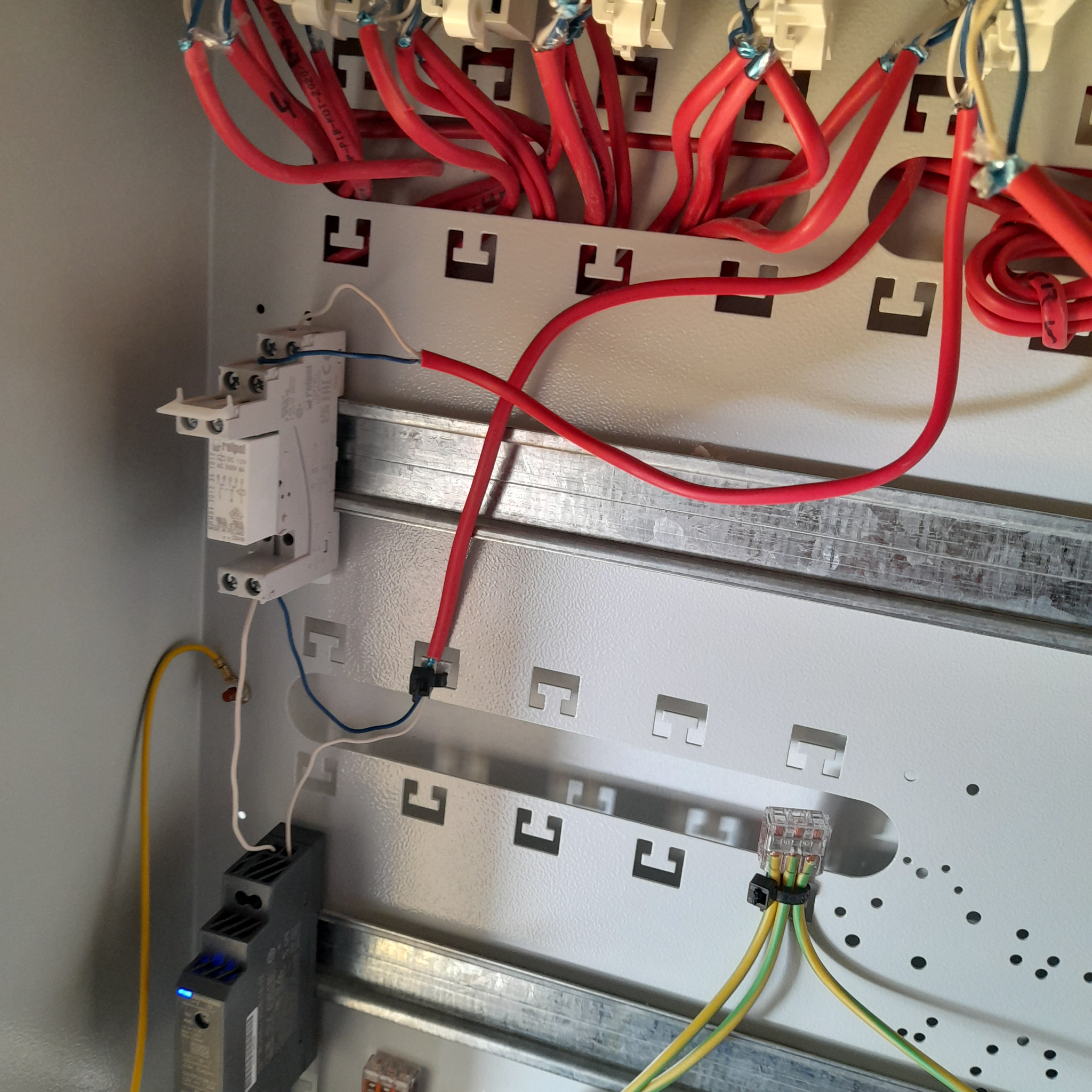 Wnętrze szafy elektrycznej z widocznymi przewodami w kolorze czerwonym, żółto-zielonym i niebieskim, zabezpieczeniami oraz listwami montażowymi.