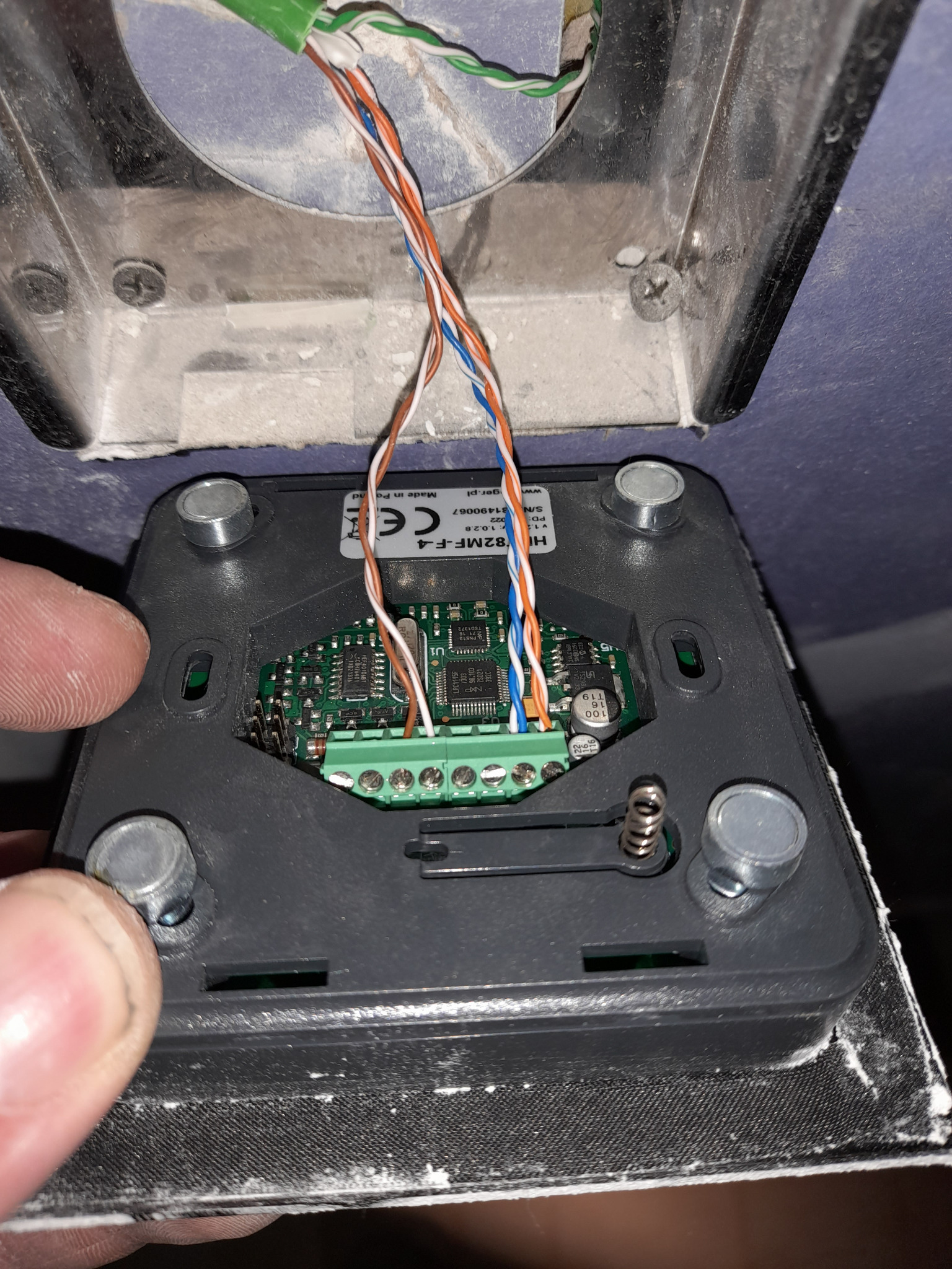 Podłączenie przewodów do listwy zaciskowej w module domofonu, widoczne elementy elektroniki na płytce drukowanej i fragment obudowy z czterema śrubami.