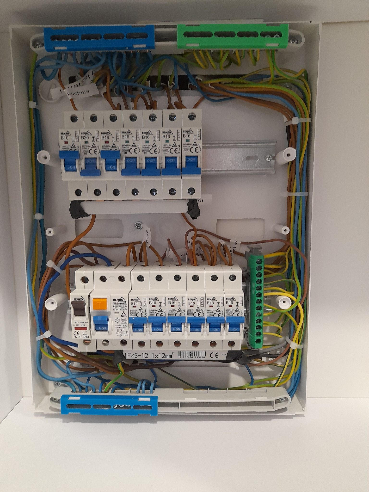 Rozdzielnica elektryczna z zamontowanymi bezpiecznikami BEMKO, okablowaniem w różnych kolorach i listwami zaciskowymi, widoczne oznaczenia 'Kuchnia' oraz parametry techniczne.