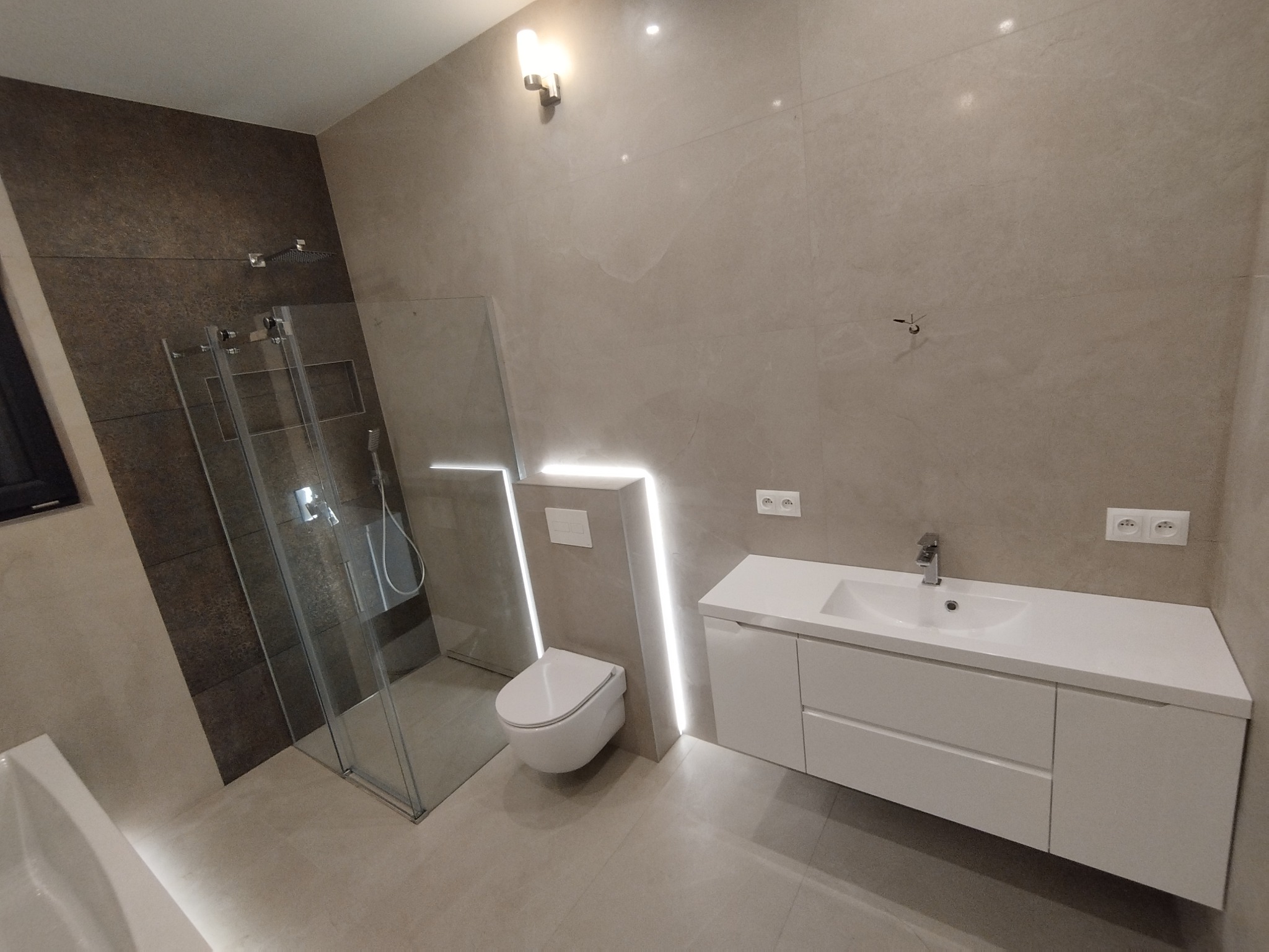 Nowoczesna łazienka z kabiną prysznicową typu walk-in, podwieszaną toaletą i białą szafką z umywalką, oświetlona paskami LED.