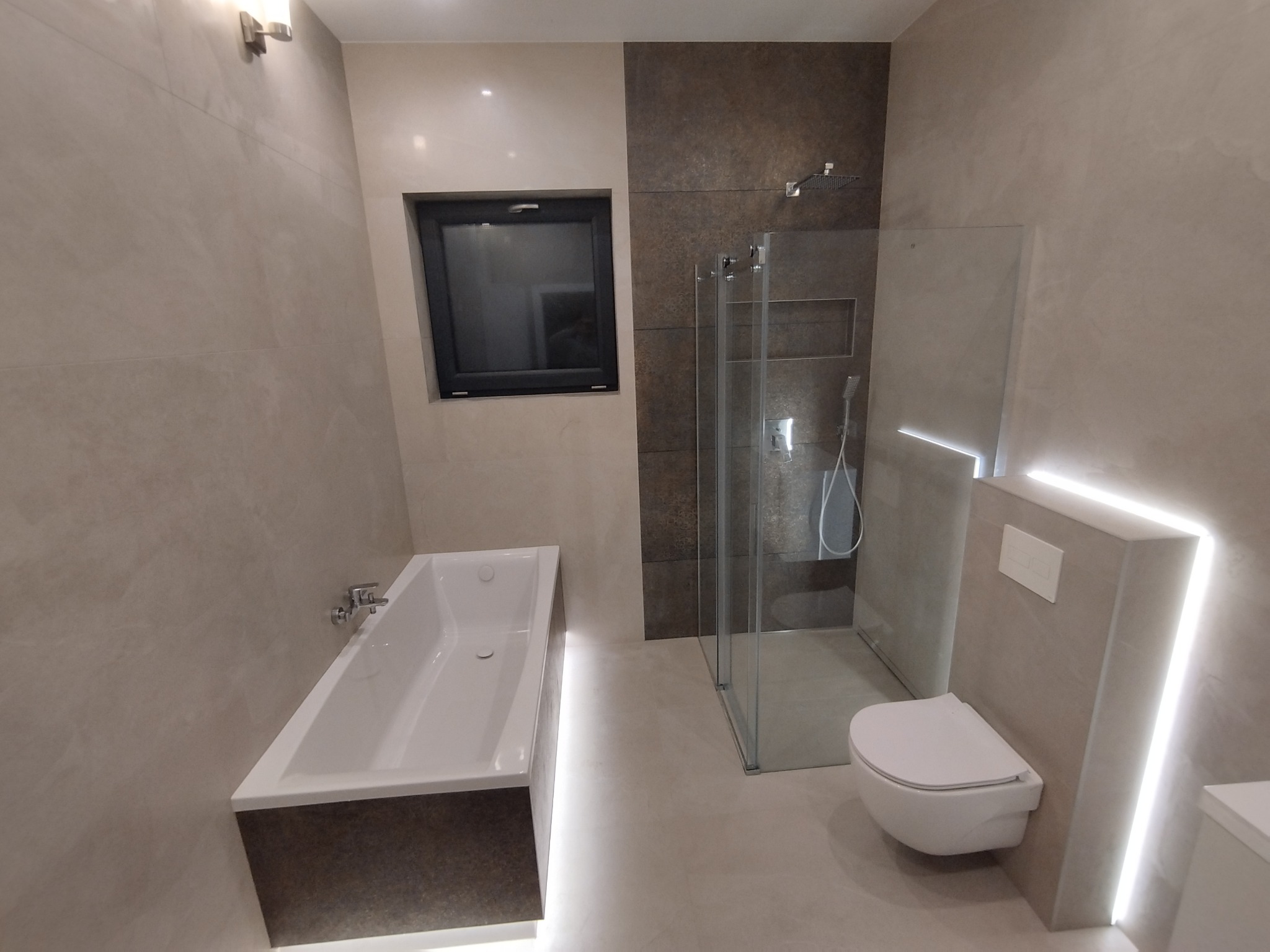 Nowoczesna łazienka z podświetlaną wanną, kabiną prysznicową typu walk-in i wiszącą toaletą, wykończona płytkami w odcieniach beżu i brązu z czarnym oknem.