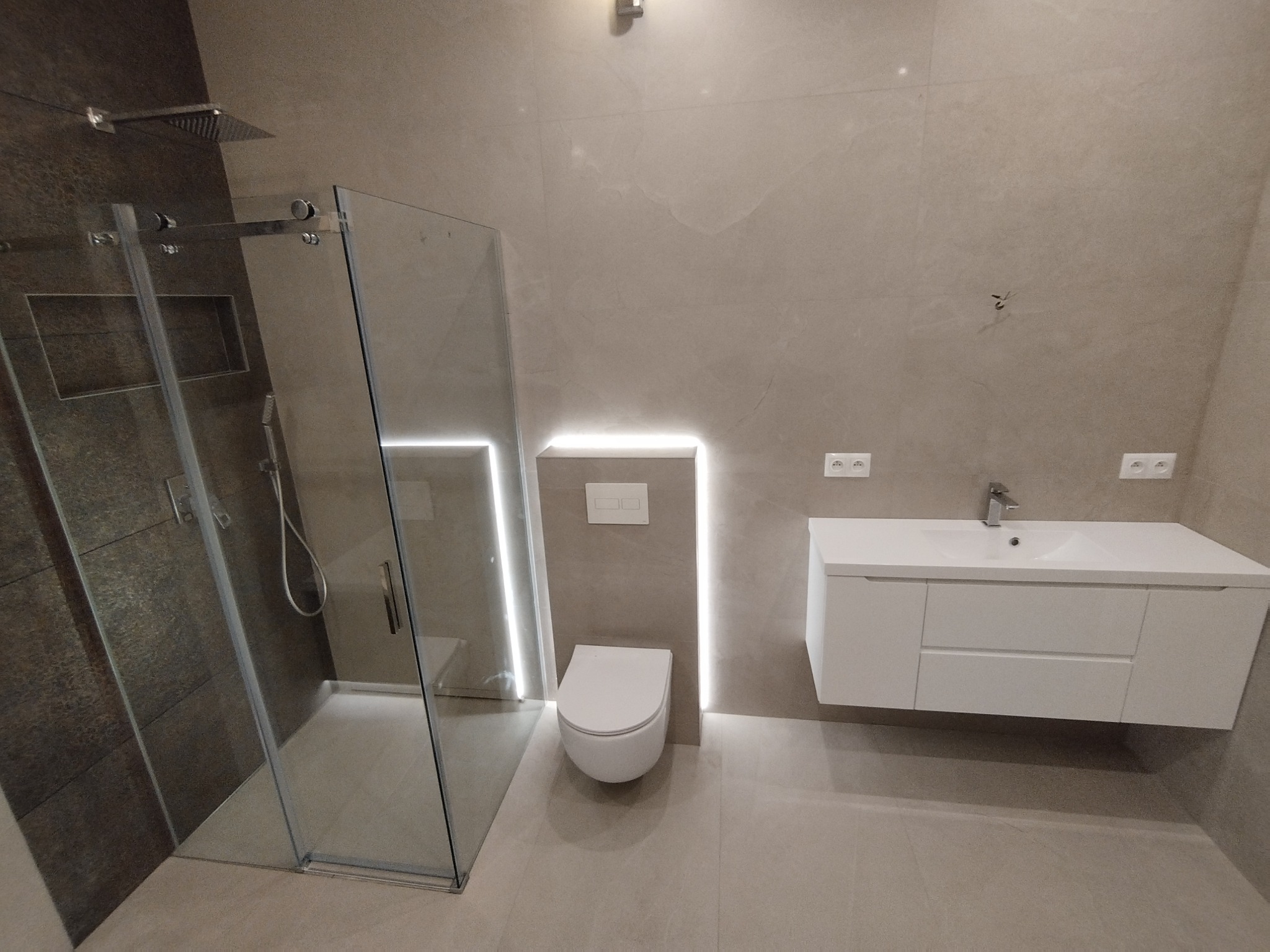 Nowoczesna łazienka z kabiną prysznicową typu walk-in, podwieszaną toaletą z podświetleniem LED, oraz białą szafką z umywalką.