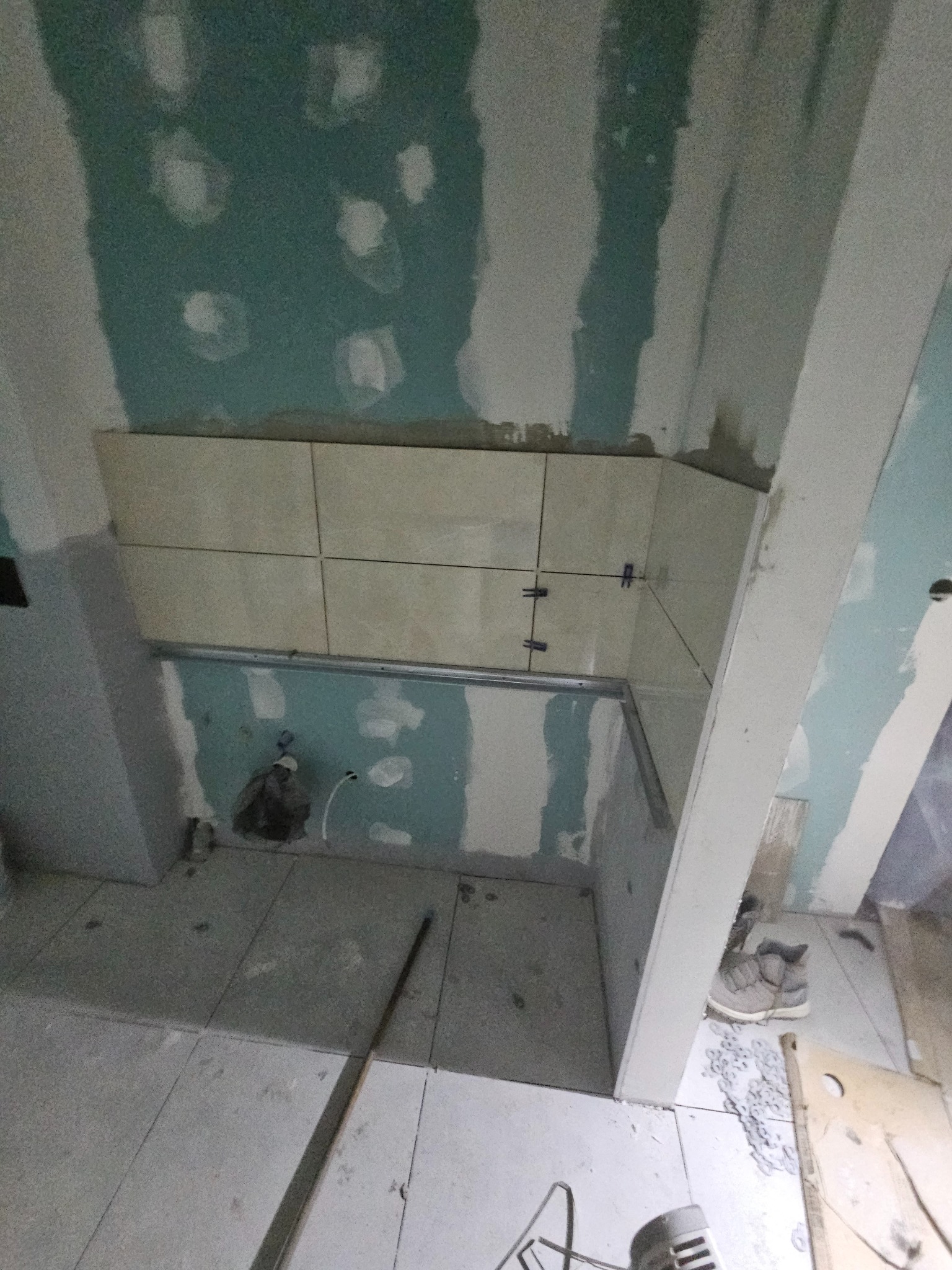 Ściana w trakcie układania płytek ceramicznych, widoczne krzyżyki dystansowe, surowy stan wykończenia ścian i podłogi, instalacja podtynkowa.